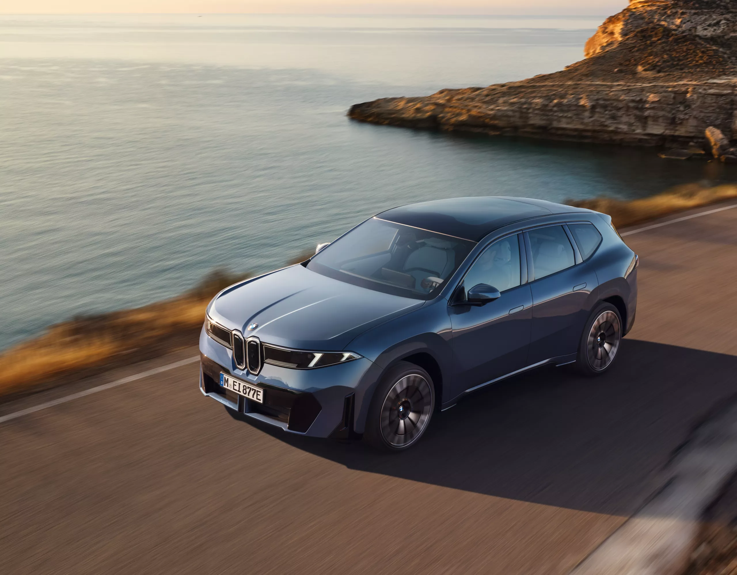 Une voiture de société électrique BMW iX3 parcourt une route côtière au lever du soleil, illustrant la mobilité durable et les solutions de flotte efficaces et zéro émission
