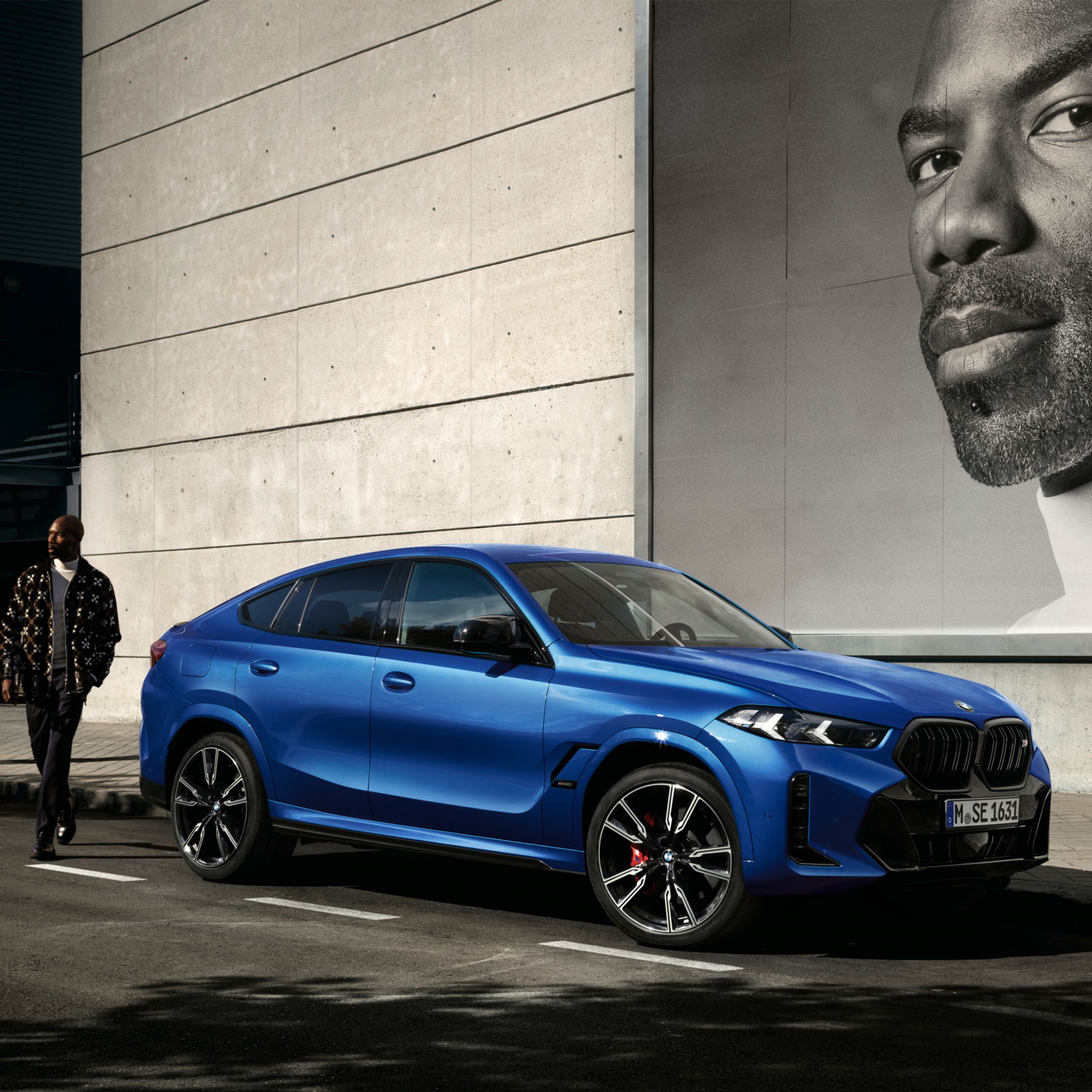 Een man nadert een BMW X6 die voor een modern gebouw geparkeerd staat