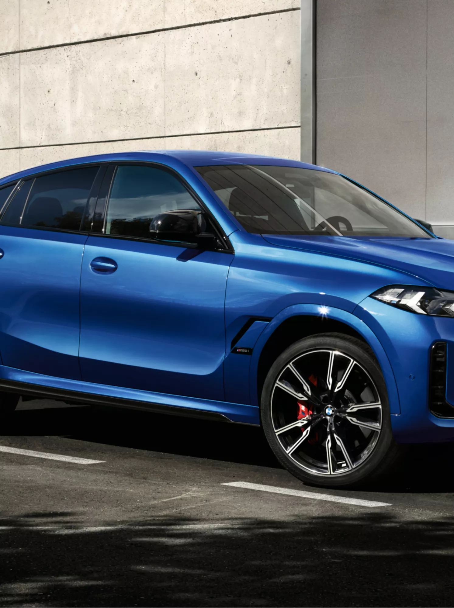 A man approaches a BMW X6 parked in front of a modern building