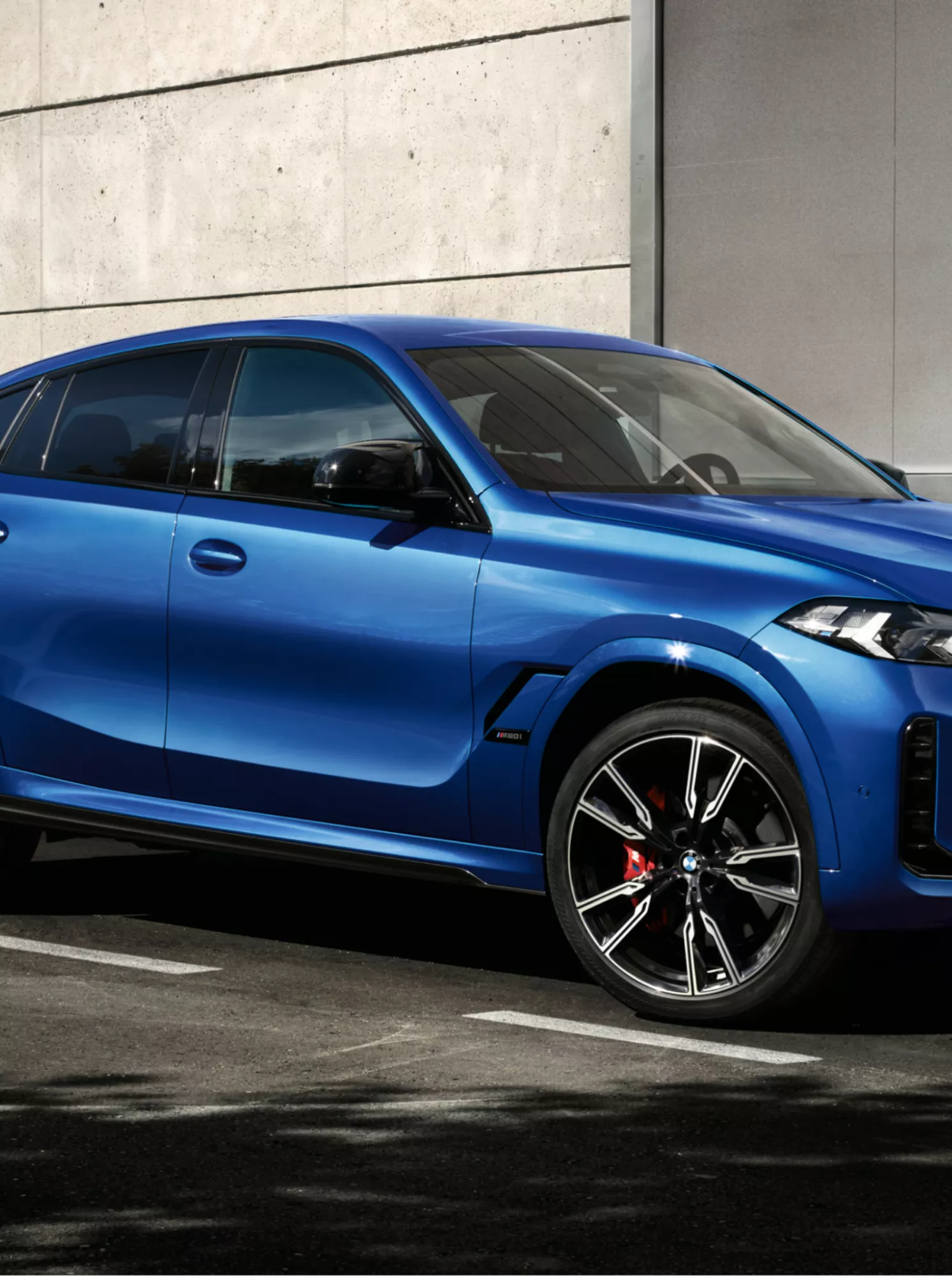 A man approaches a BMW X6 parked in front of a modern building