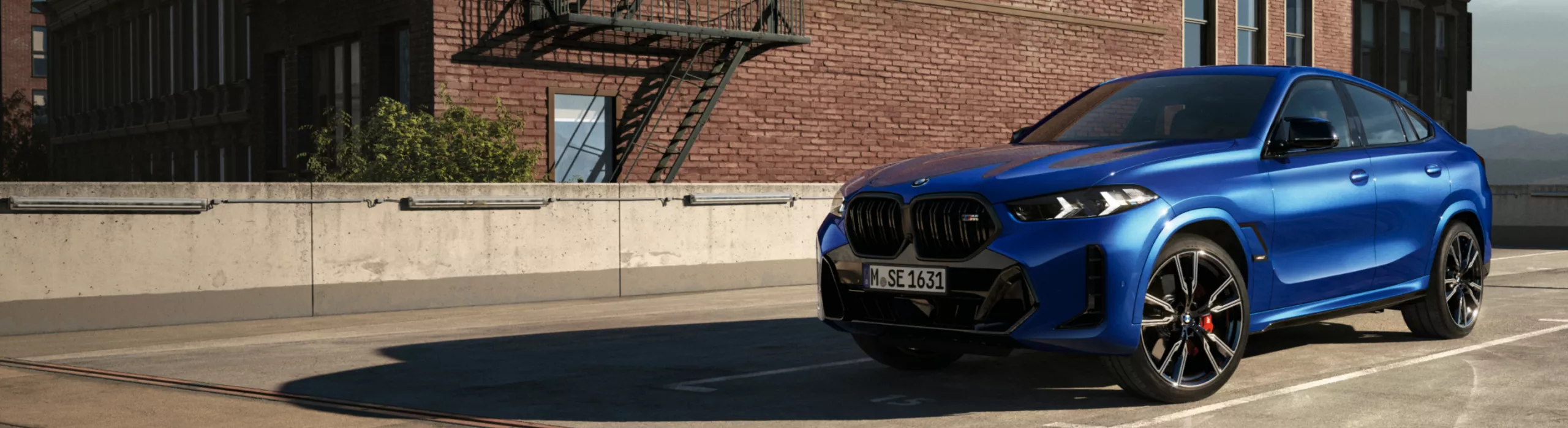 Un BMW X6 SUV este parcat în lumina soarelui în fața unei clădiri din cărămidă