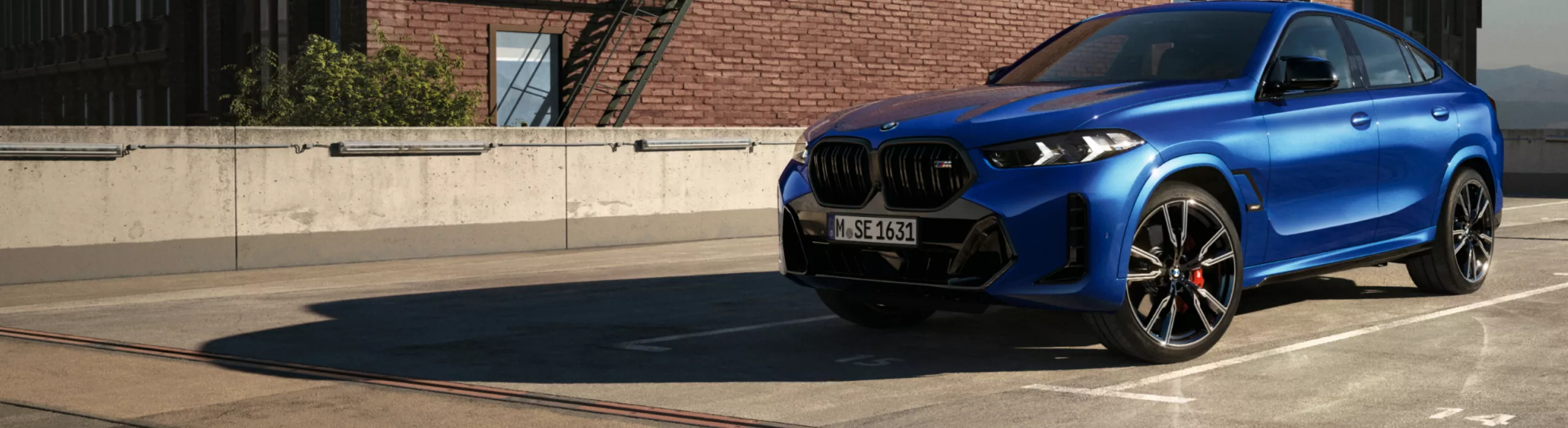 Ein BMW X6 SUV steht im Sonnenlicht auf einem Parkplatz vor einem Ziegelsteingebäude 