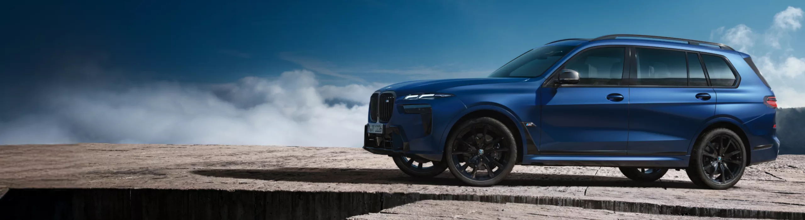 Ein BMW X7 M60i xDrive steht auf einem Steinplateau unter blauem Himmel