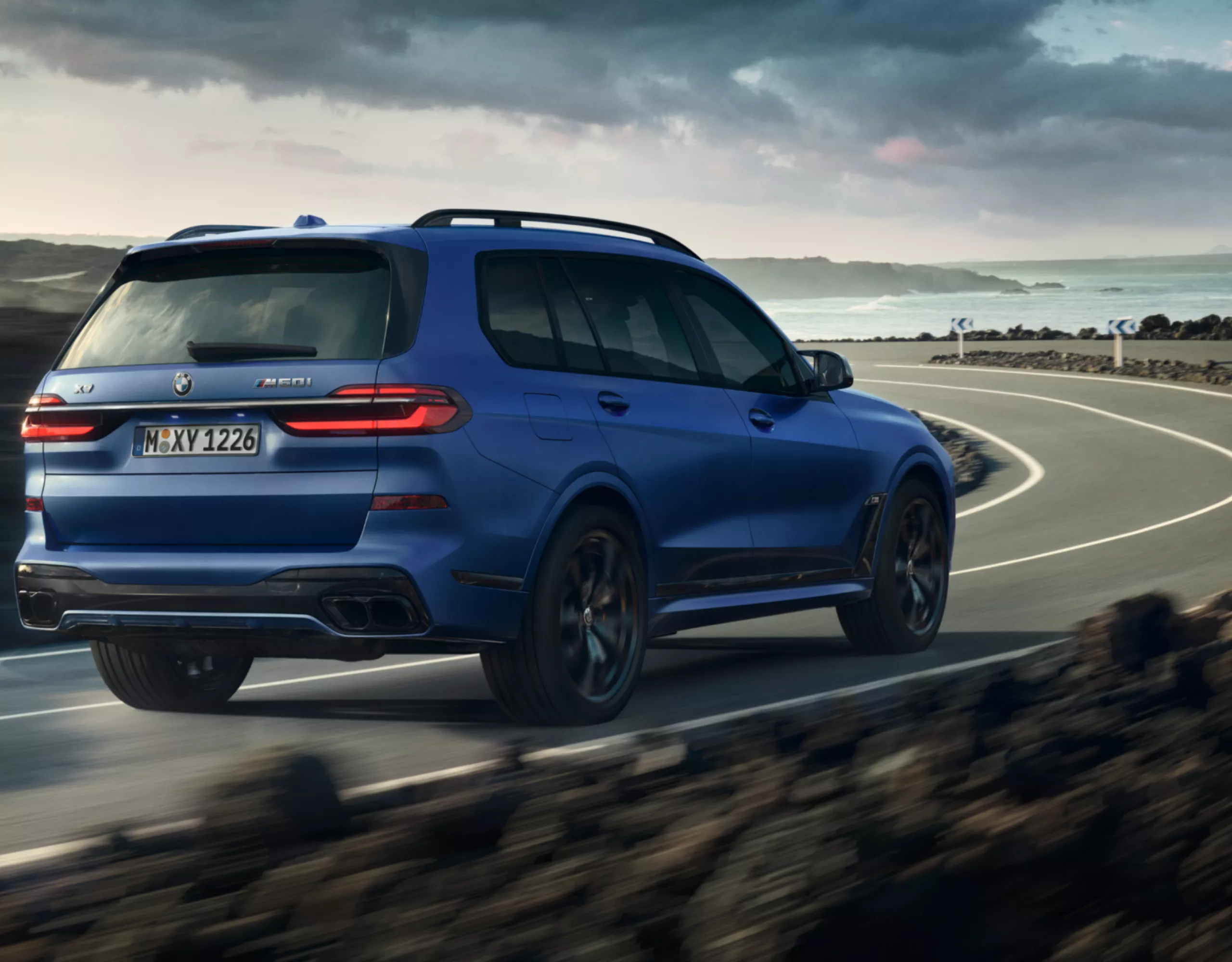 Une BMW X7 M60i xDrive roule sur une route sinueuse le long de la côte