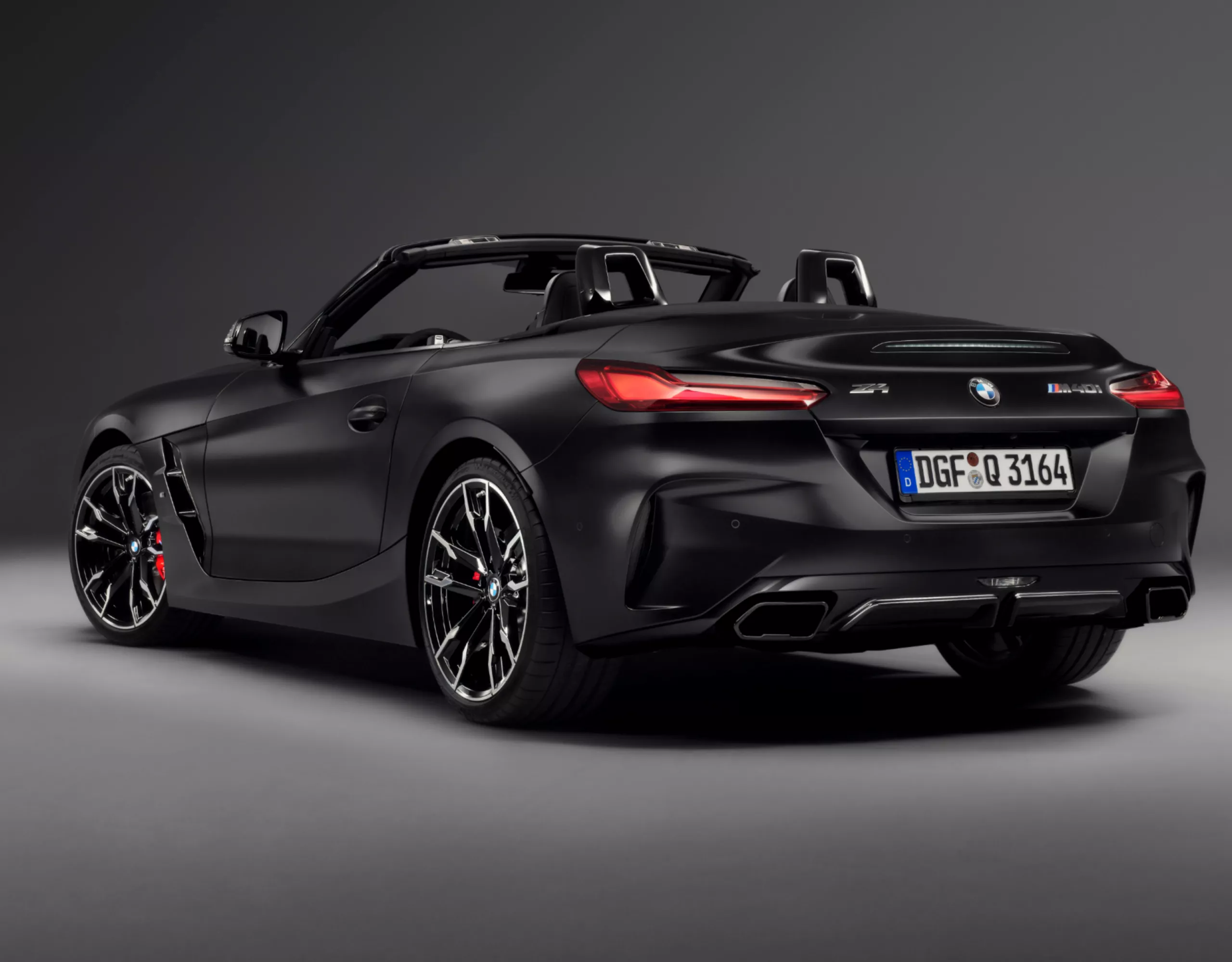 Vue arrière de la BMW Z4 M40i Roadster Final Edition avec toit ouvert, peinture métallisée BMW Individual Frozen Black et sorties d’échappement noires