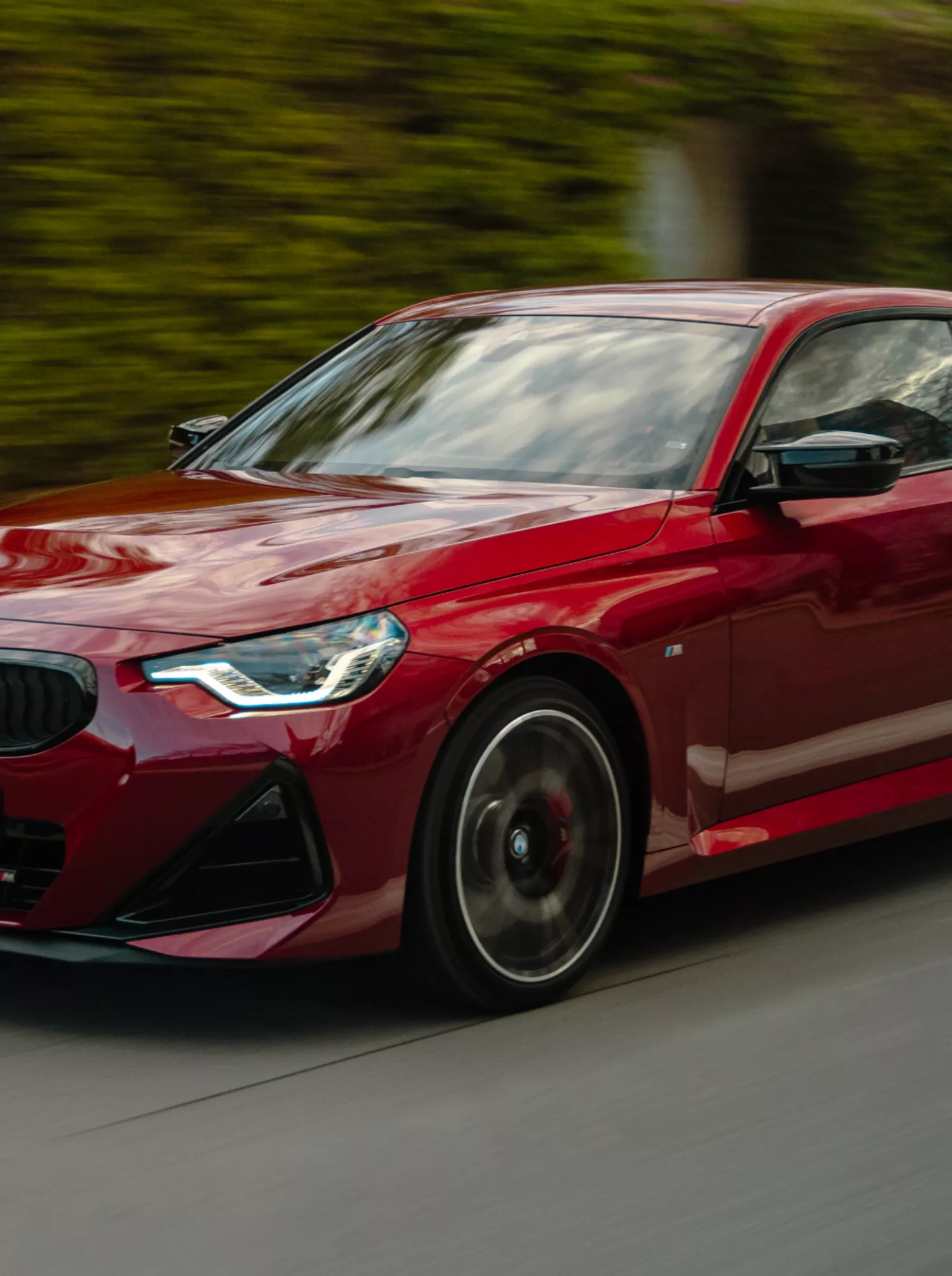BMW 2 Series Coupé drives in town in front of a green house wall