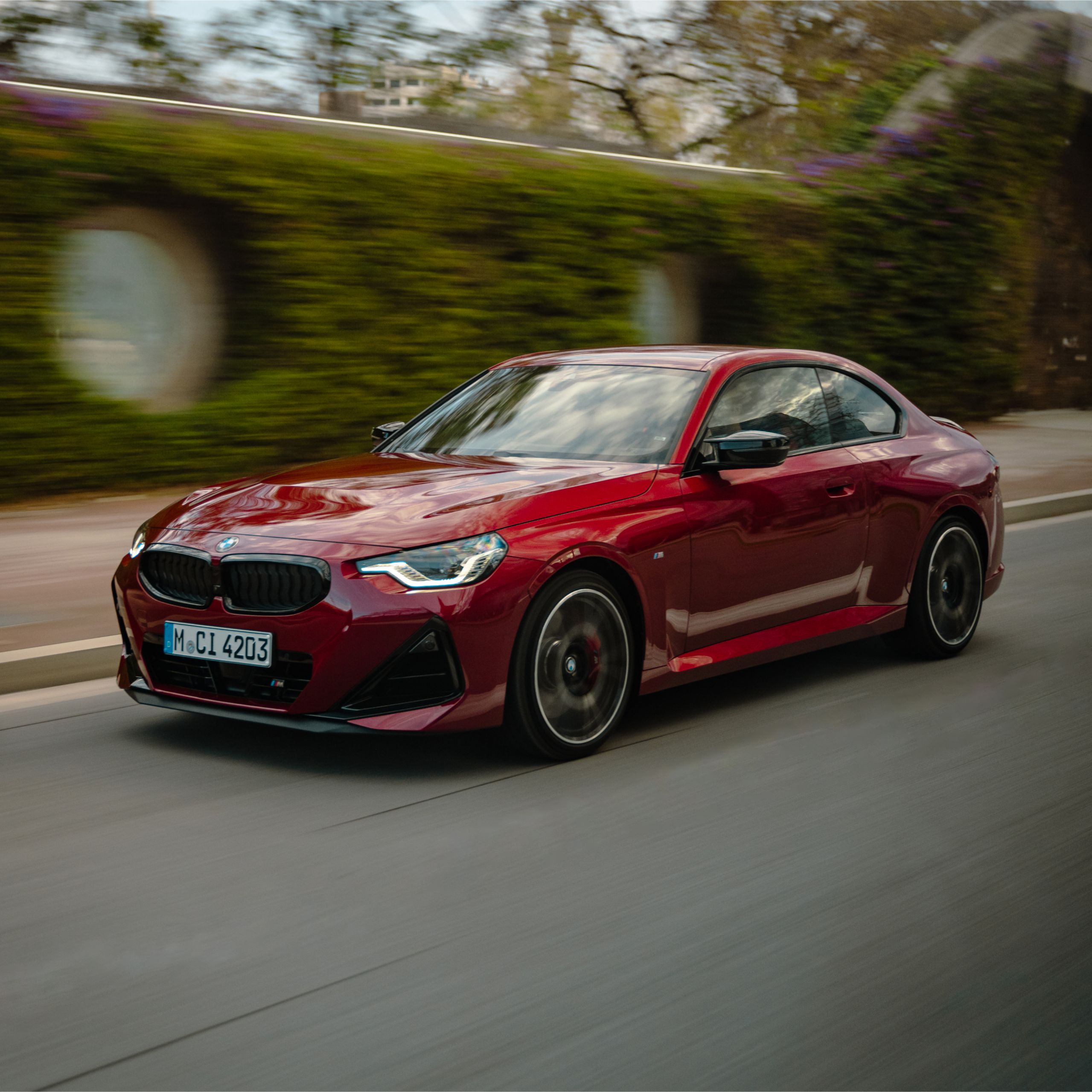 BMW serii 2 Coupé jedzie przez miasto na tle zielonej ściany domów