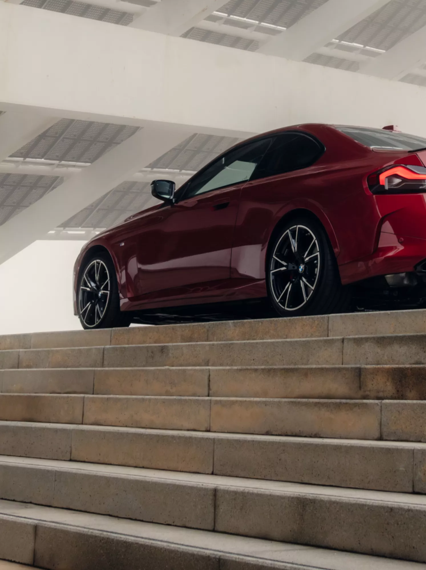 Eine Person steigt eine breite Treppe hinauf an deren Ende ein BMW 2er Coupé parkt