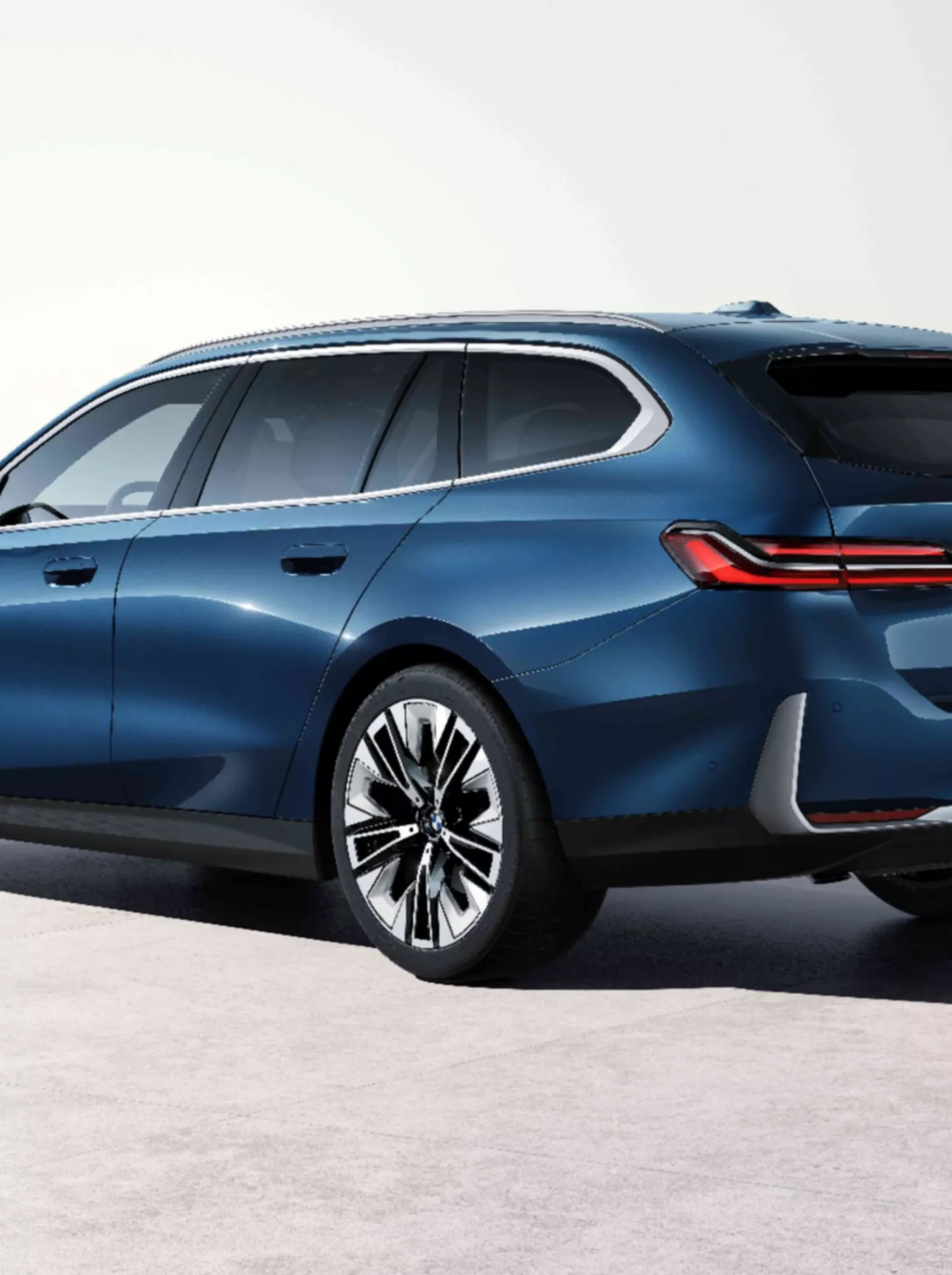 BMW i5 Touring показано от заден три-четвърти ъгъл пред светла стена