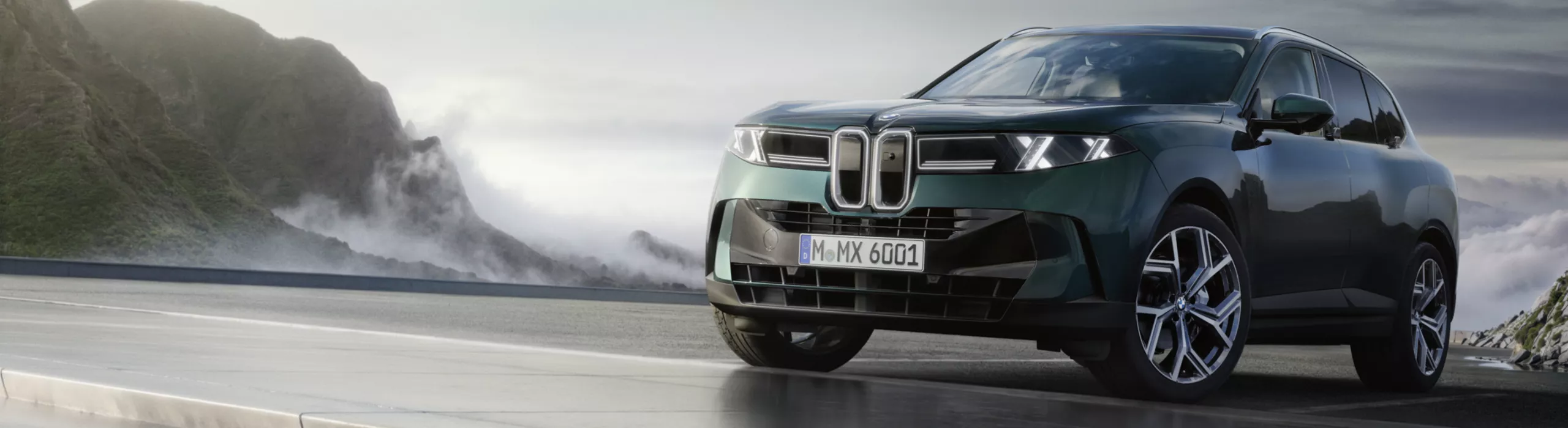 Vpravo je zaparkované BMW X5. V pozadí jsou vidět hory a působivá obloha