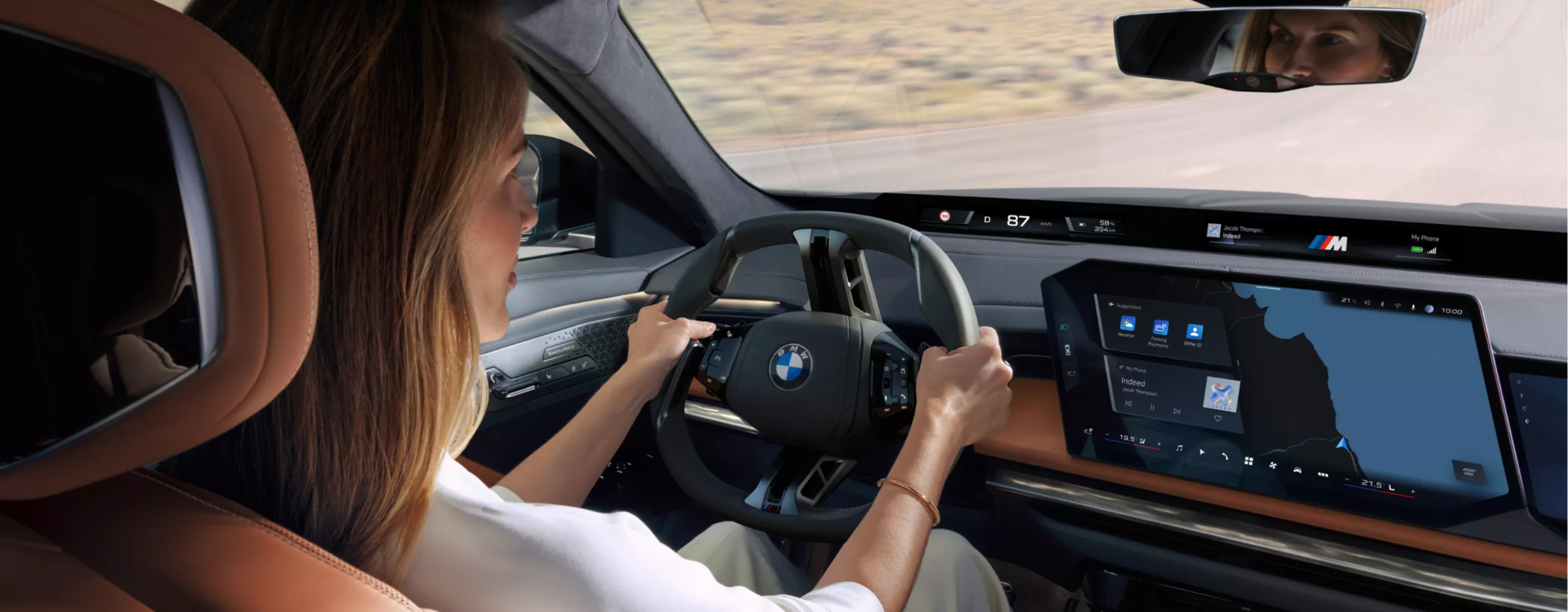 Blick von der Rücksitzbank auf die fahrende Person, das Lenkrad und das zentrale Informationsdisplay.