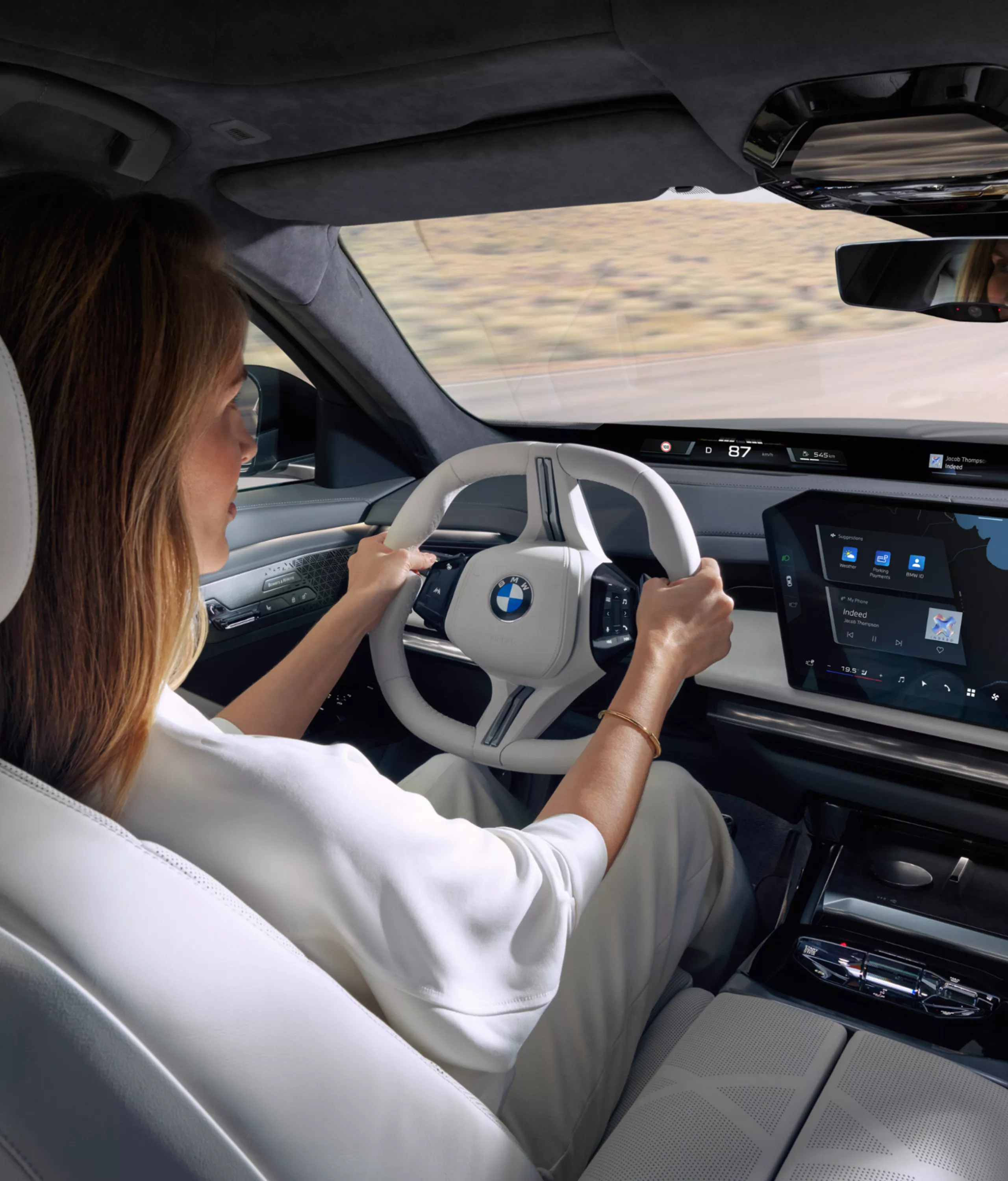 Blick von der Rücksitzbank auf die fahrende Person, das Lenkrad und das zentrale Informationsdisplay.