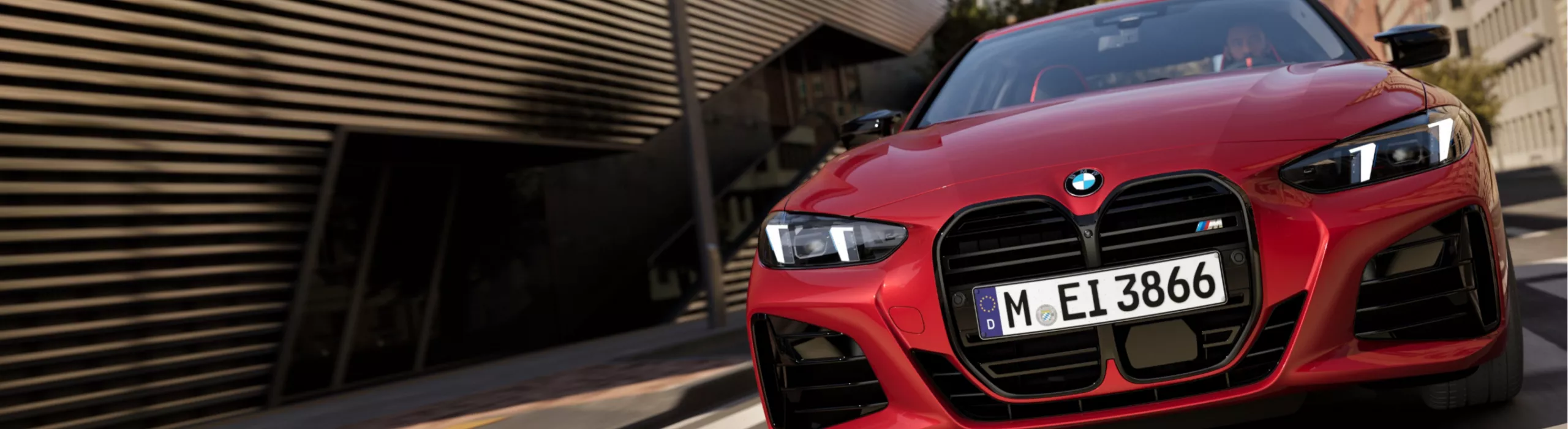 Ein roter BMW M440i xDrive mit M Badge und adaptiven LED Scheinwerfern fährt auf einer Straße in der Innenstadt