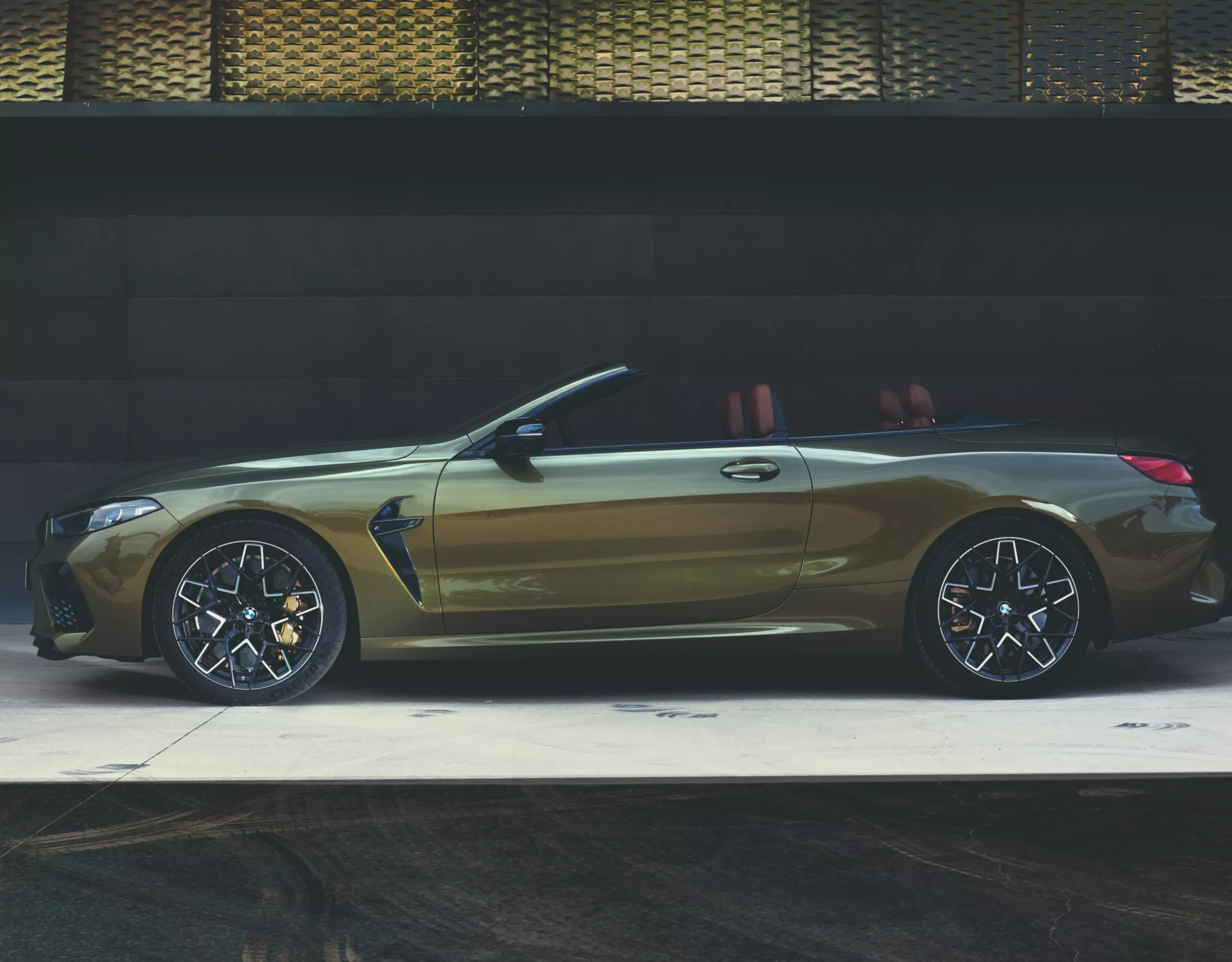 BMW M8 Competition convertible with open roof in front of metal facade