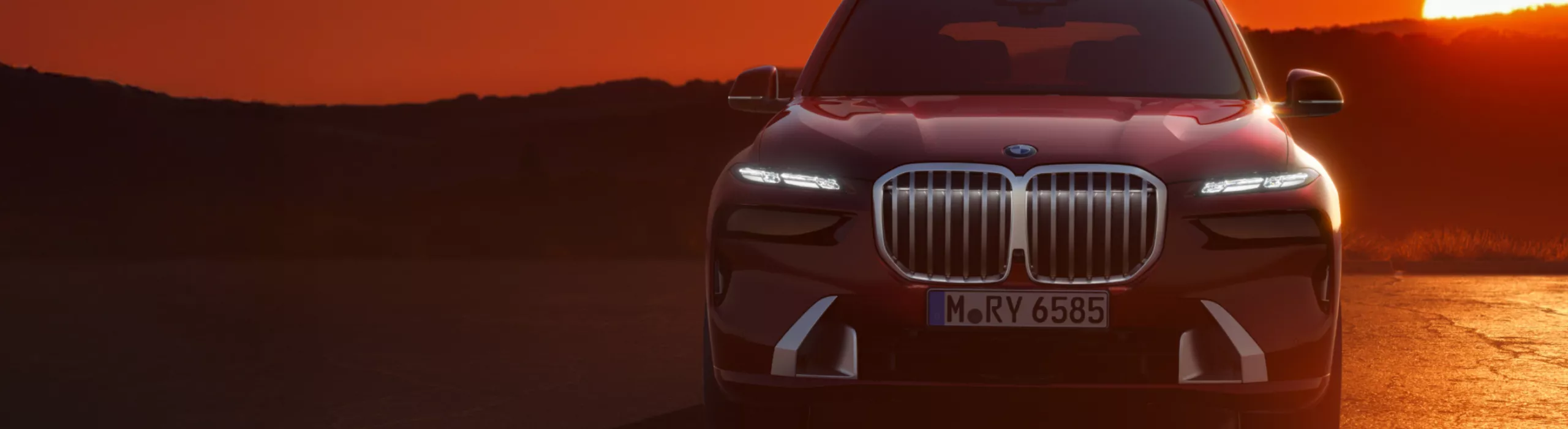 背景に丘陵地帯が広がる道で夕焼けに照らされるBMW X7