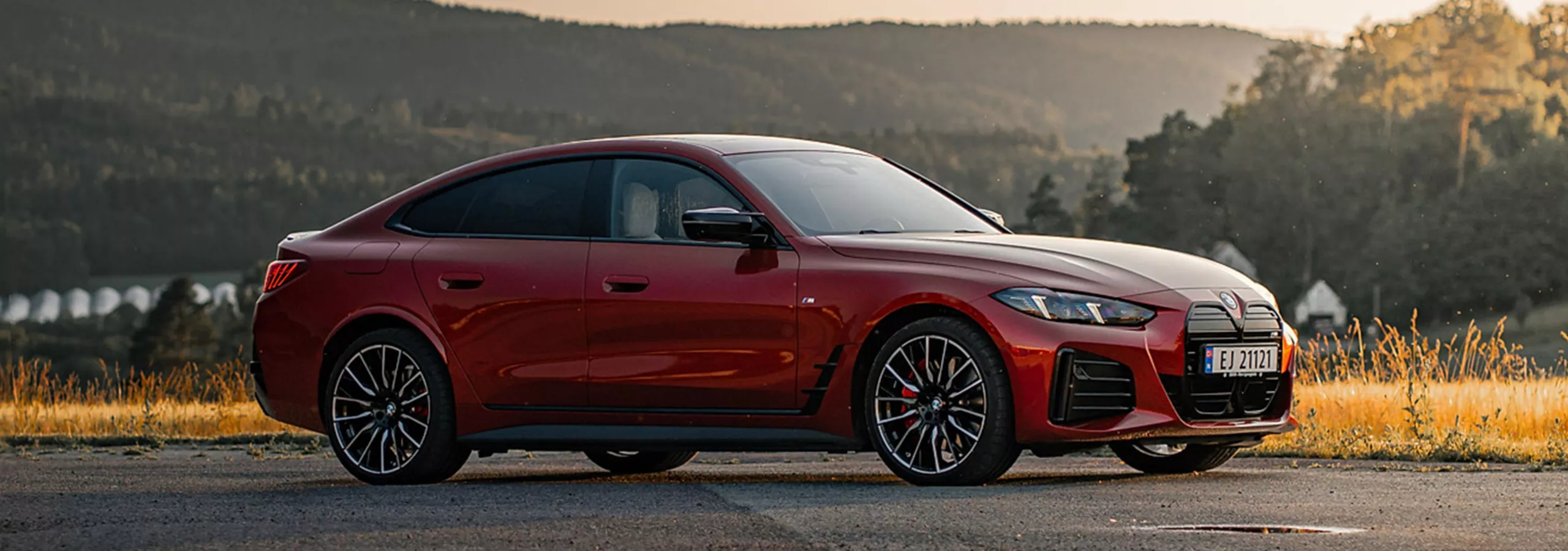 En rödfärgad BMW i4 M50 parkerad med natur i bakgrund.