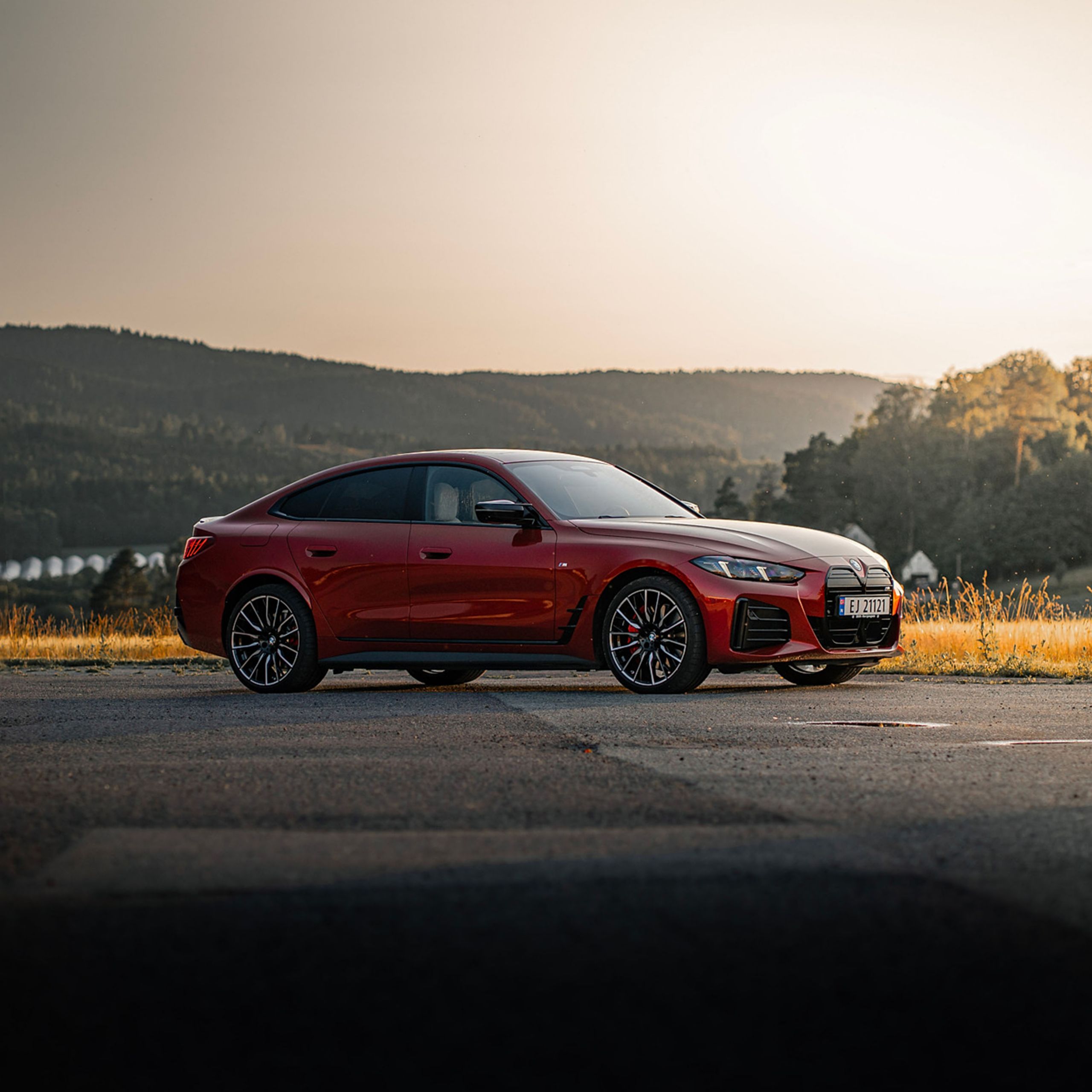 En rödfärgad BMW i4 M50 parkerad med natur i bakgrund.