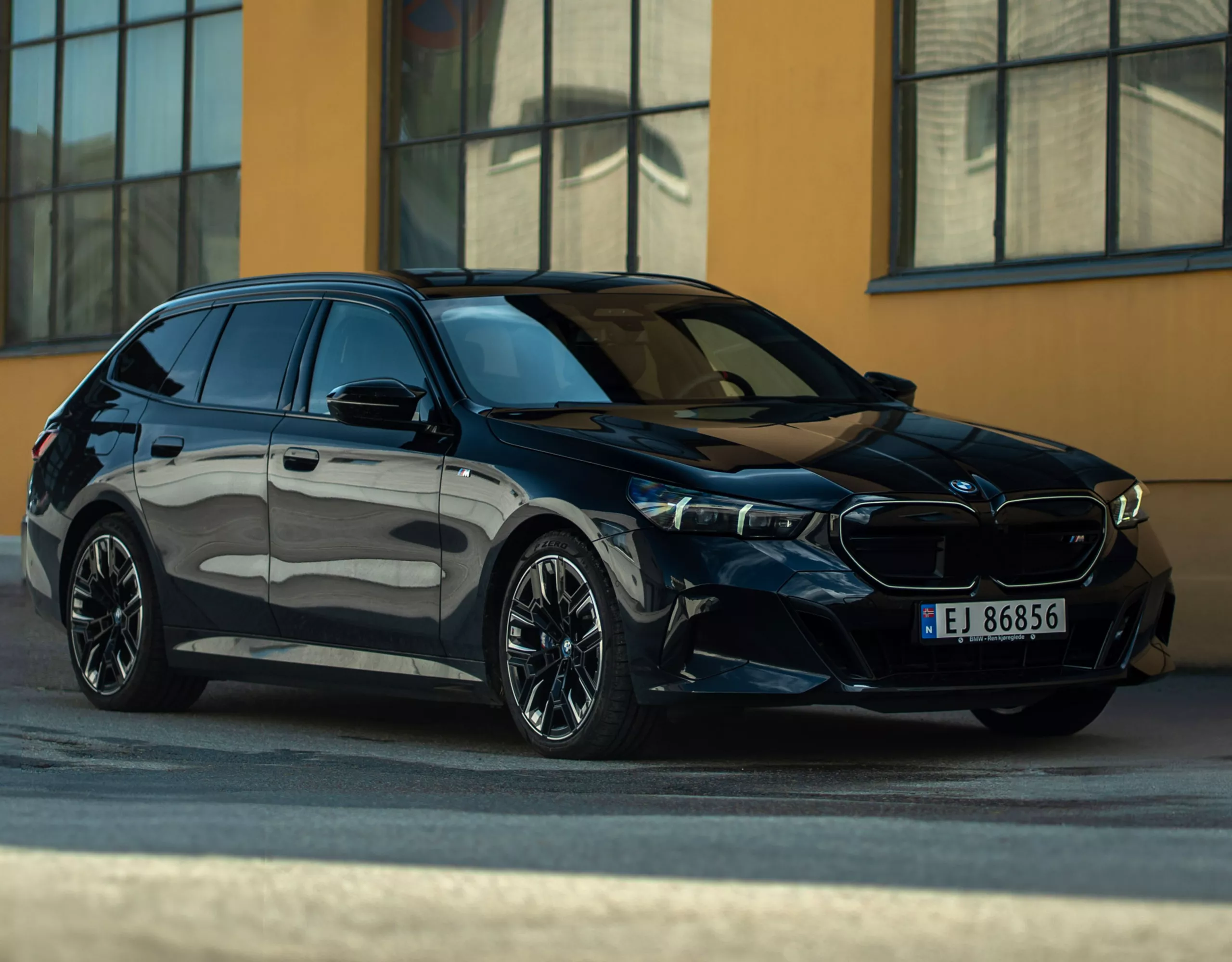 En svart BMW i5 Touring utanför en industribyggnad.