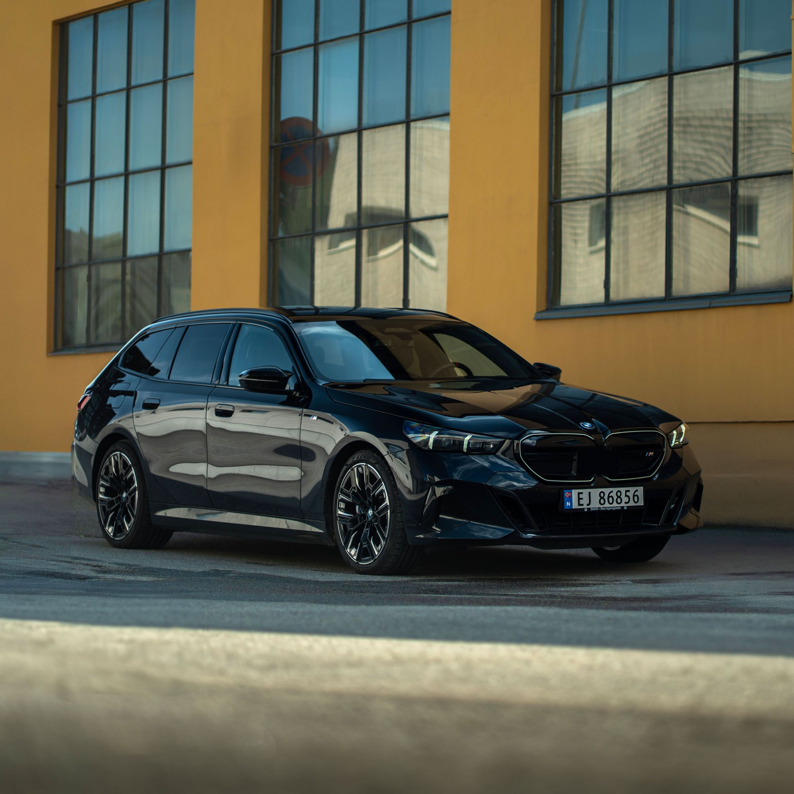 En svart BMW i5 Touring utanför en industribyggnad.