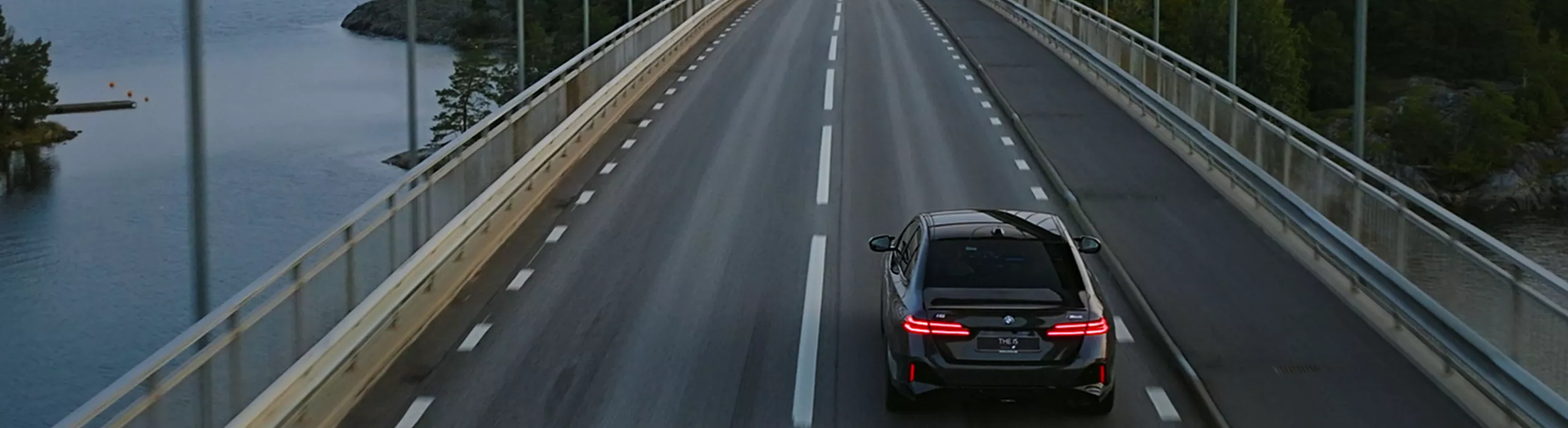 En BMW i5 som kör över en bro en fin sommardag.