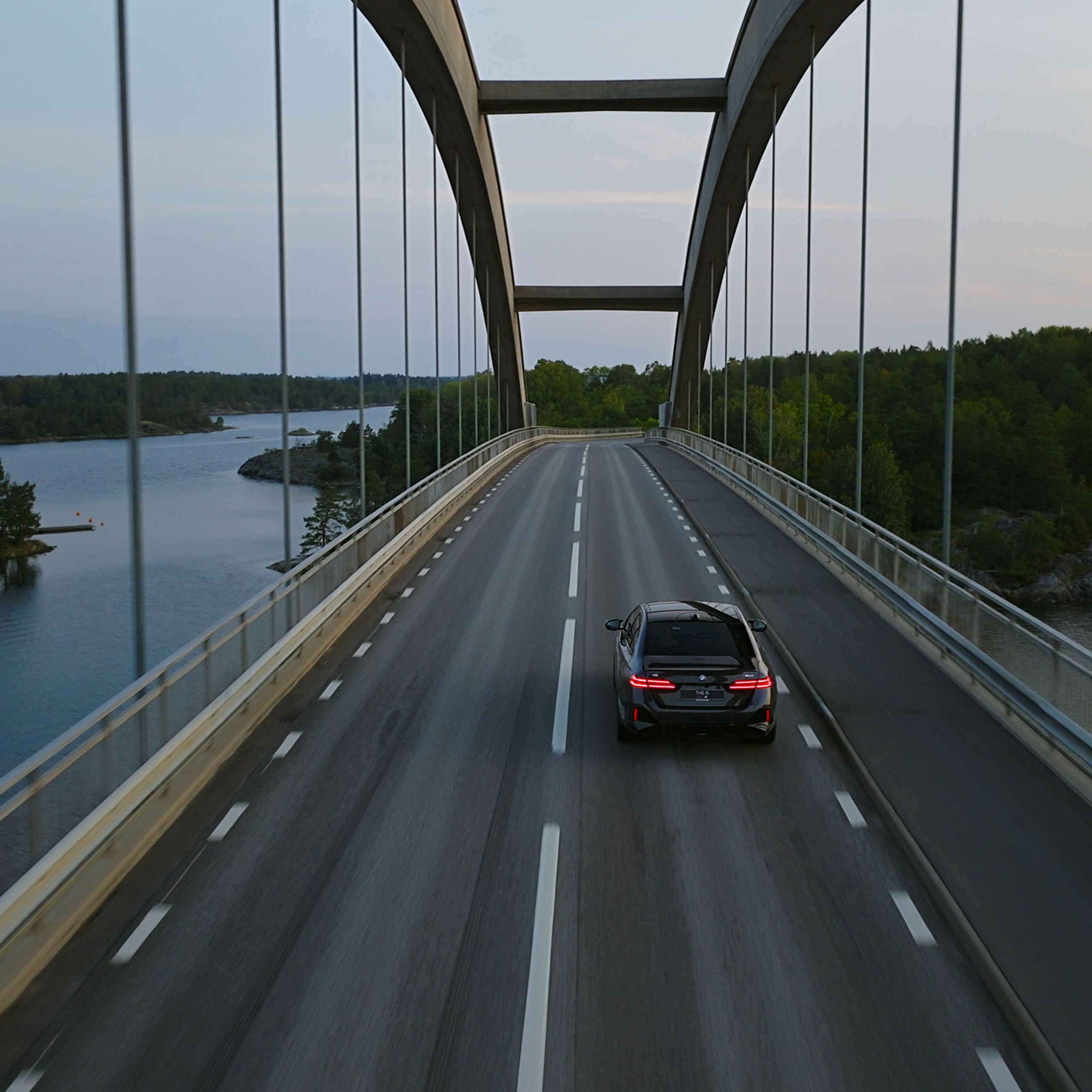 En BMW i5 som kör över en bro en fin sommardag.