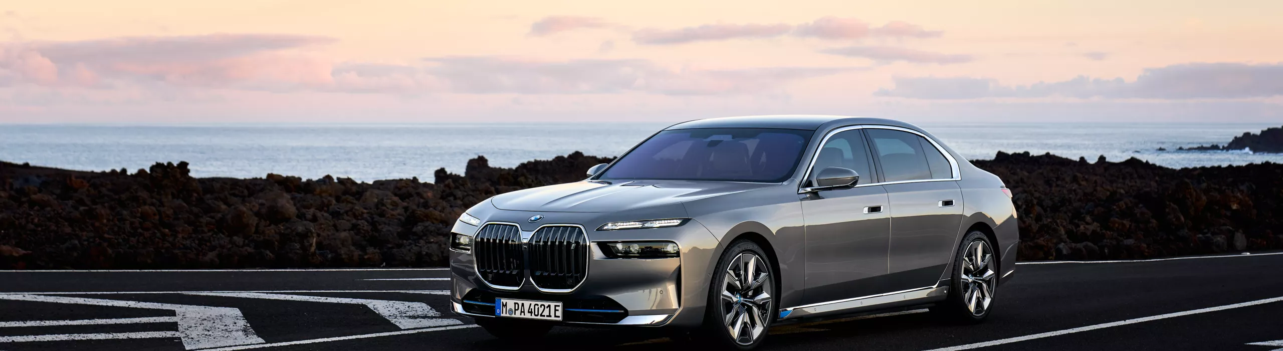 BMW i7 xDrive60 มุมมองด้านข้างรถพร้อมทิวทัศน์ขณะพระอาทิตย์ตก