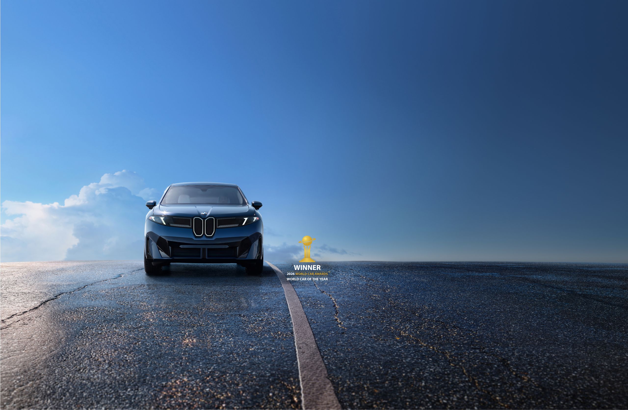 The BMW iX3 parked on a slick road in front of a blue sky with the 2026 World Car Awards' World Car of the Year logo and text in the bottom right corner.