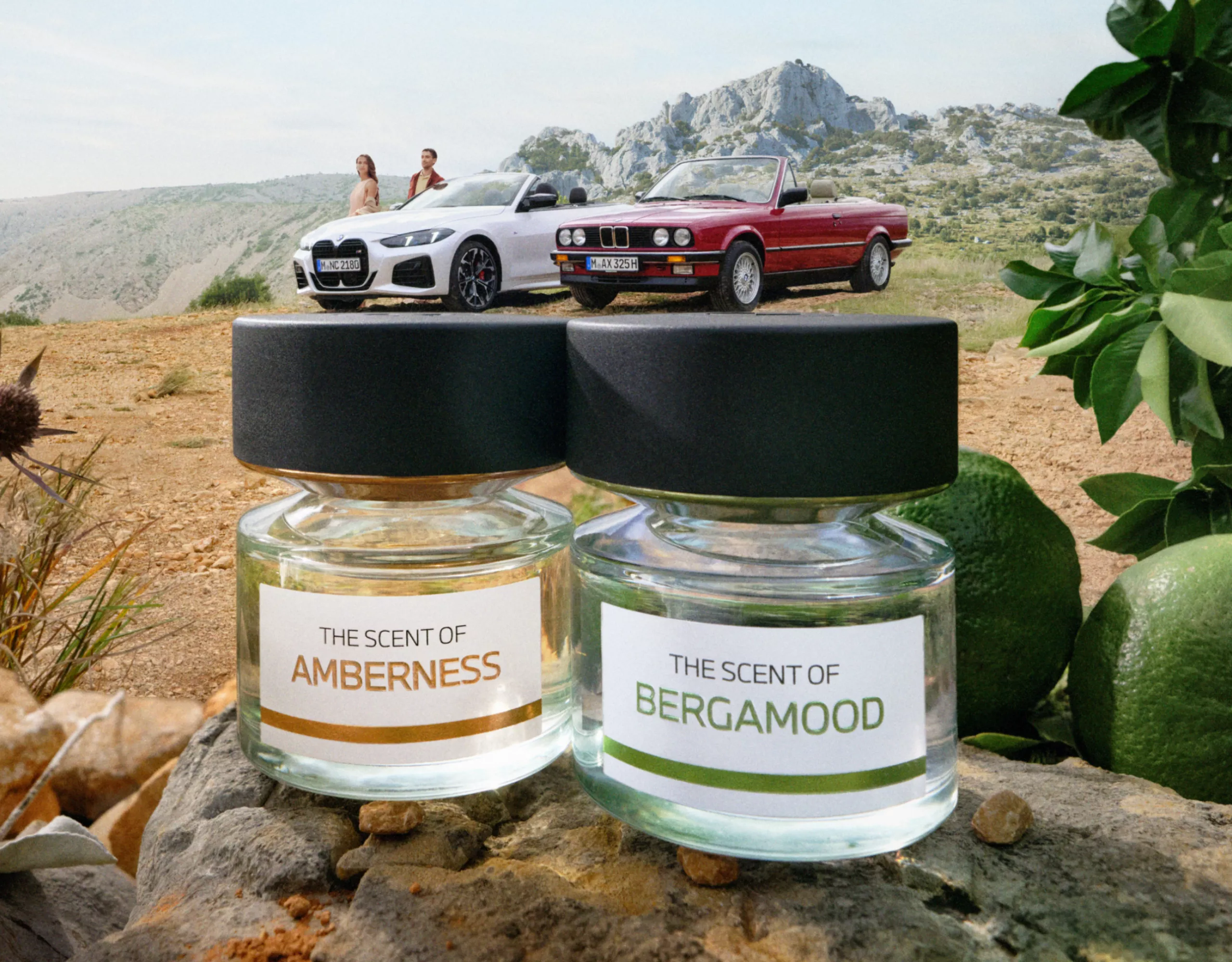 BMW Lifestyle Fragrances Amberness und Bergamood abgebildet in einer Landschaft vor zwei BMW Autos