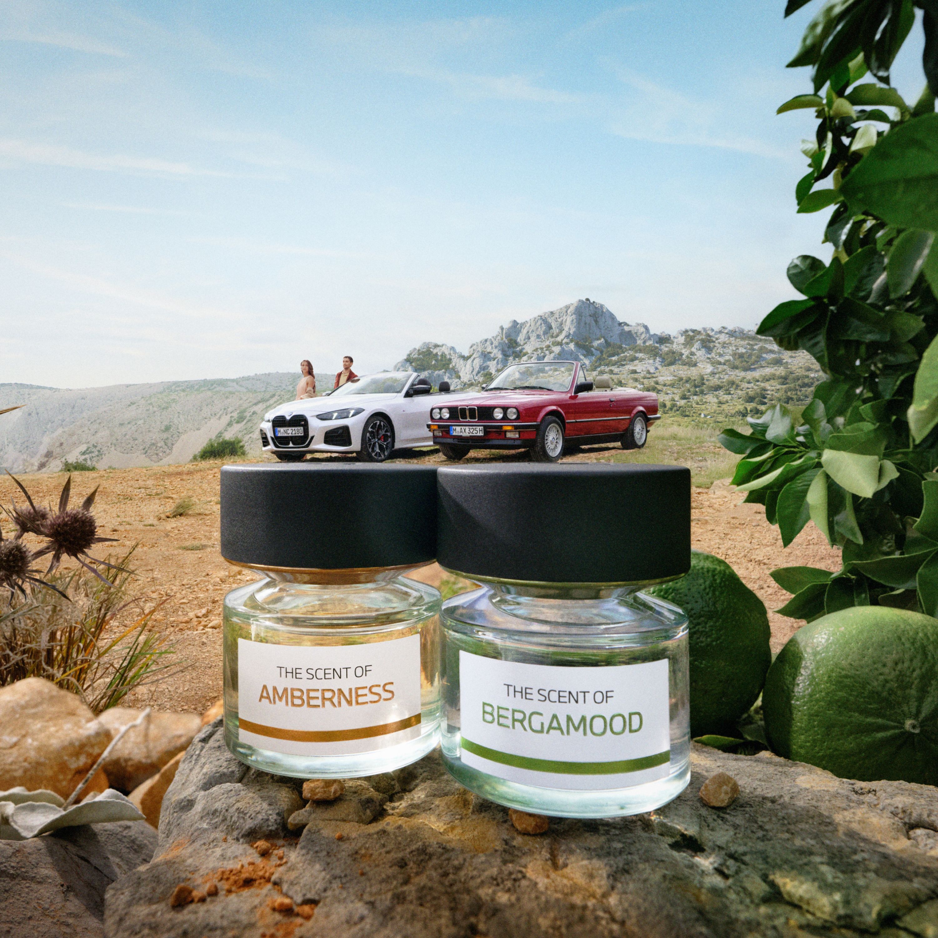 I profumi BMW Lifestyle Amberness e Bergamood fotografati con un paesaggio sullo sfondo davanti a due auto BMW