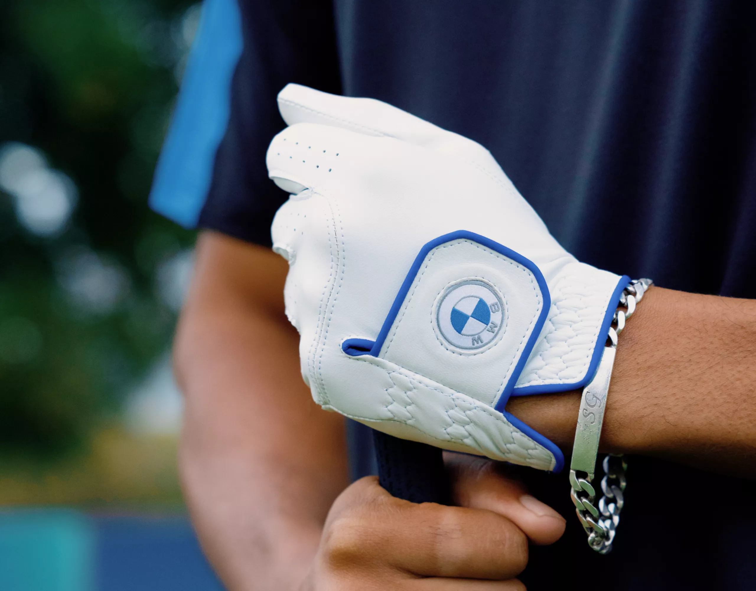 White golf gloves with blue BMW logo, detail, worn by a person holding a golf club
