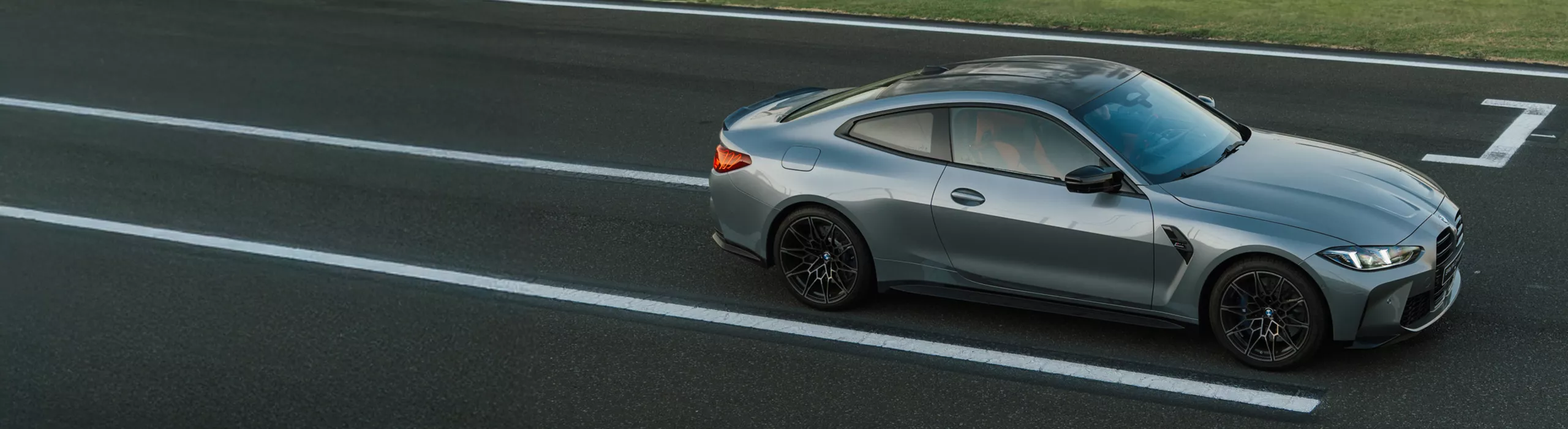 Vista externa do BMW M4 Competition Coupé sobre uma ponte de concreto molhada que atravessa um canal.