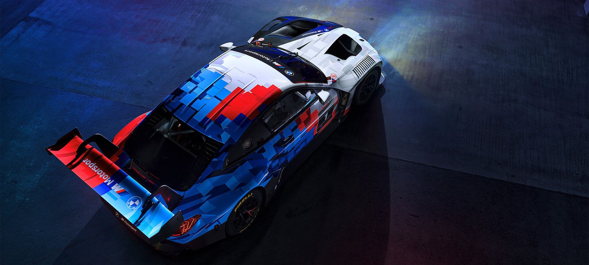 Ein roter sportlicher BMW fährt über eine Schotterstraße in einer grün bewachsenen Landschaft. 