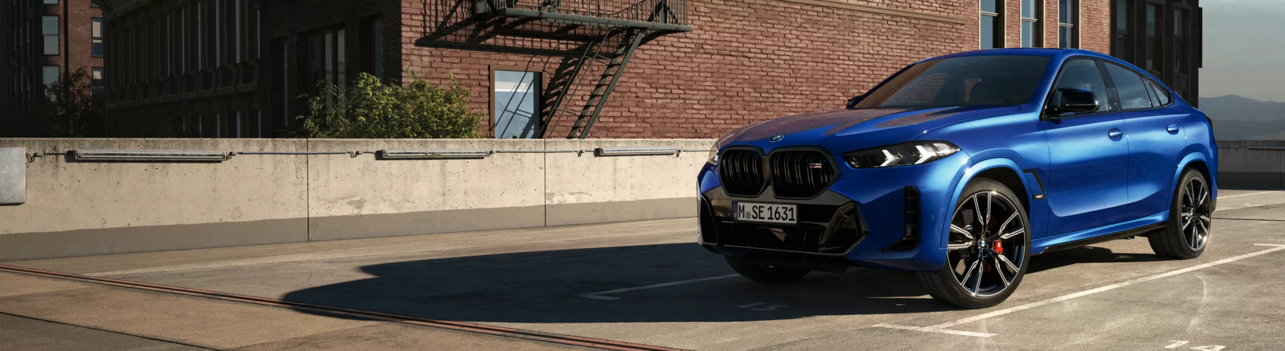 A BMW X6 SUV Highlights is parked in the sunlight in front of a brick building