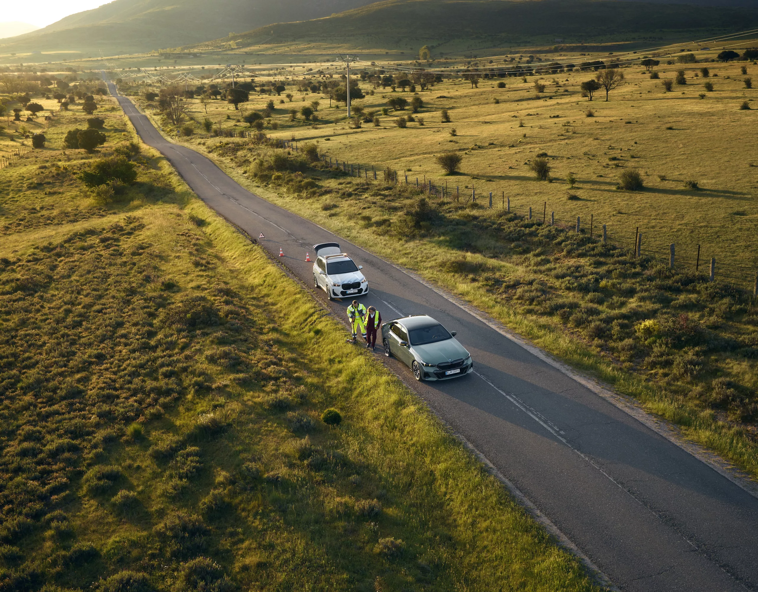 A group of people with backpacks and helmets approach a climbing wall. Next to them is a parked BMW