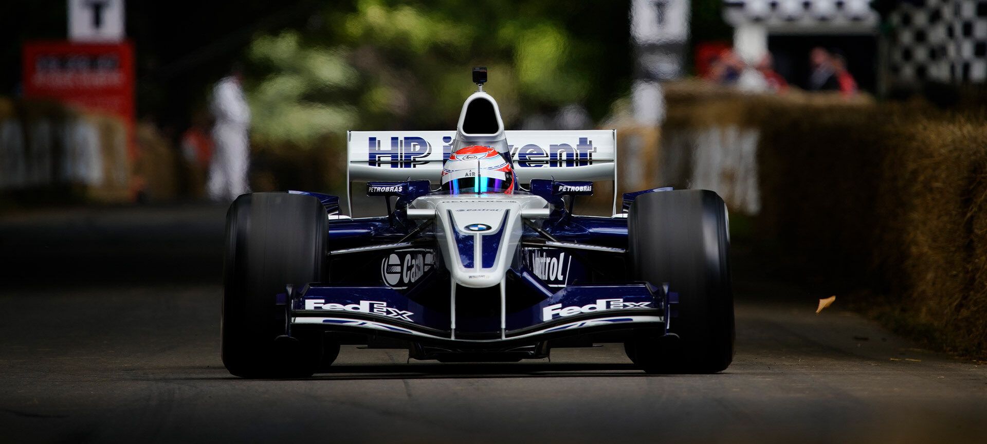 Ein roter sportlicher BMW fährt über eine Schotterstraße in einer grün bewachsenen Landschaft. 