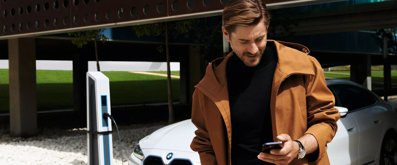 Homem a usar o telemóvel junto a um BMW ligado a um carregador elétrico