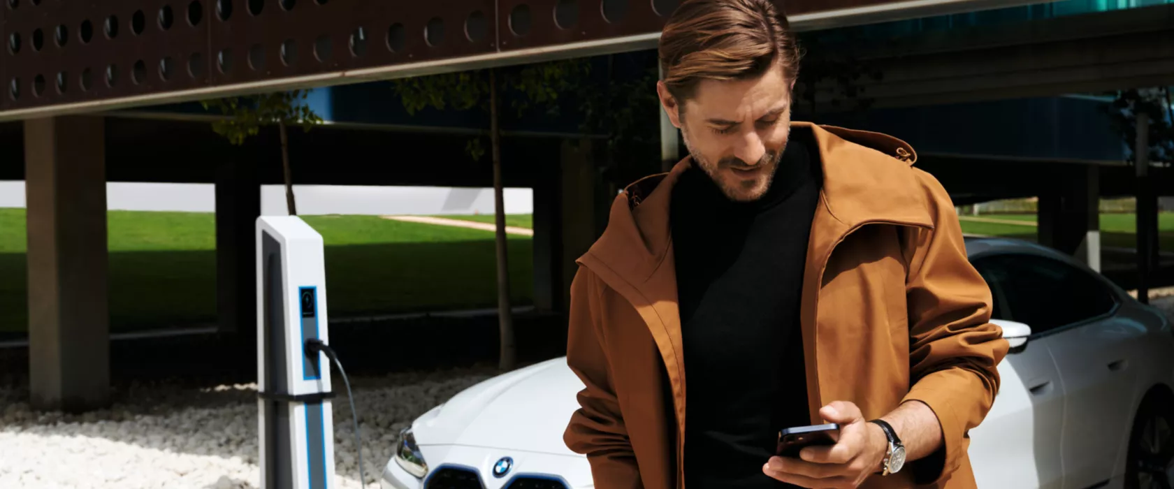 Man in front of BWW iX uses My BMW app on smartphone