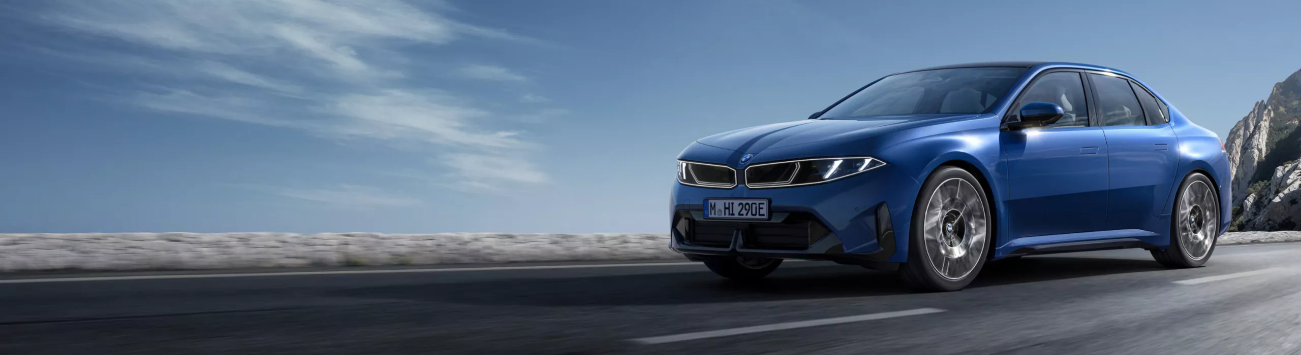 A BMW i3 Sedan is driving on a curvy serpentine road through the mountains