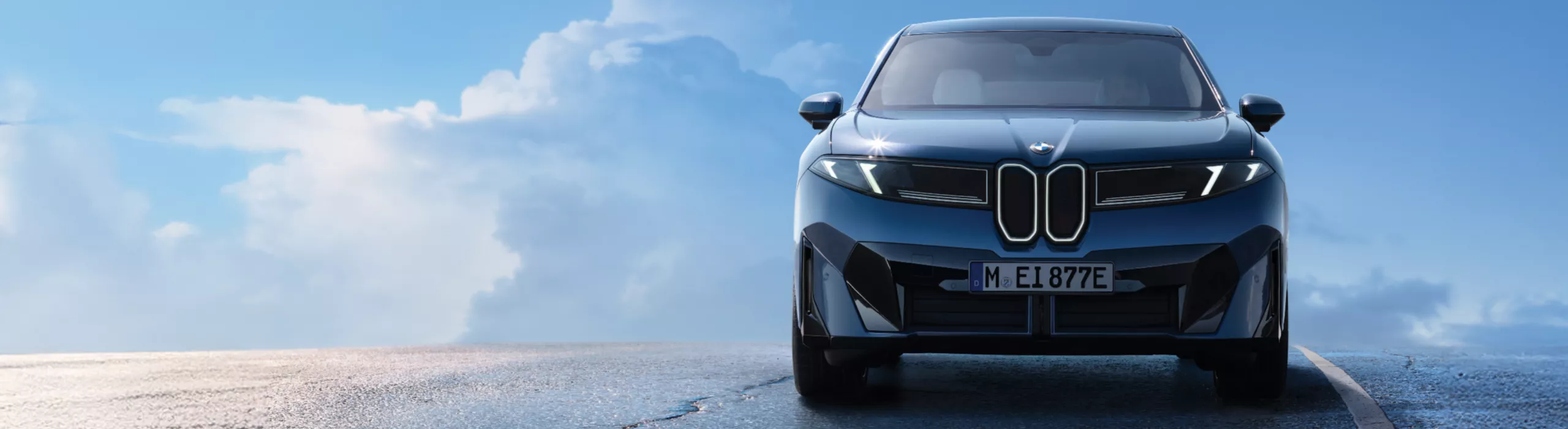 뭉게 구름이 있는 화창한 하늘을 향한 젖은 노면을 달리고 있는 BMW iX3