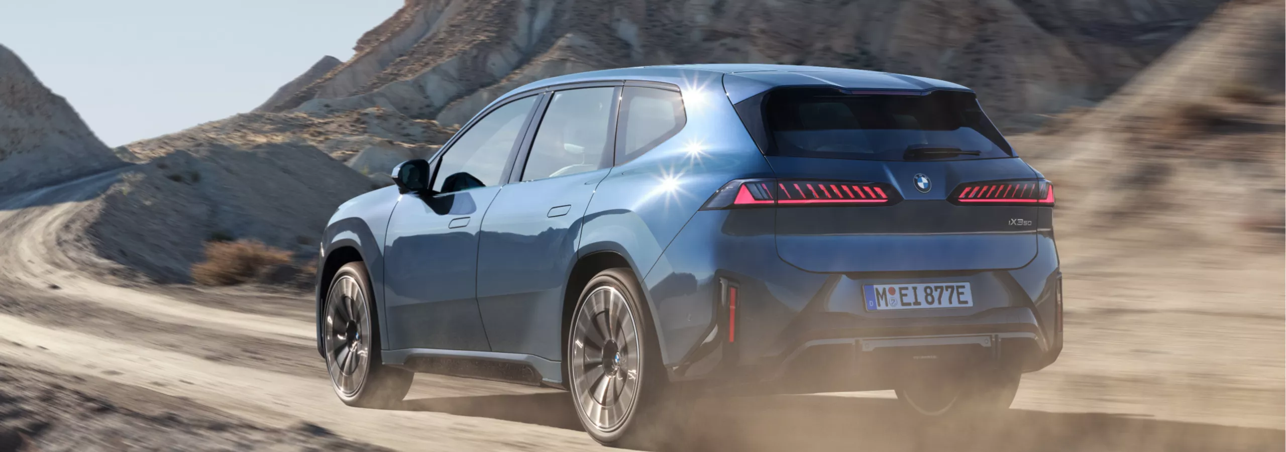 BMW iX3 едет по гравийной дороге в скалистой горной местности
