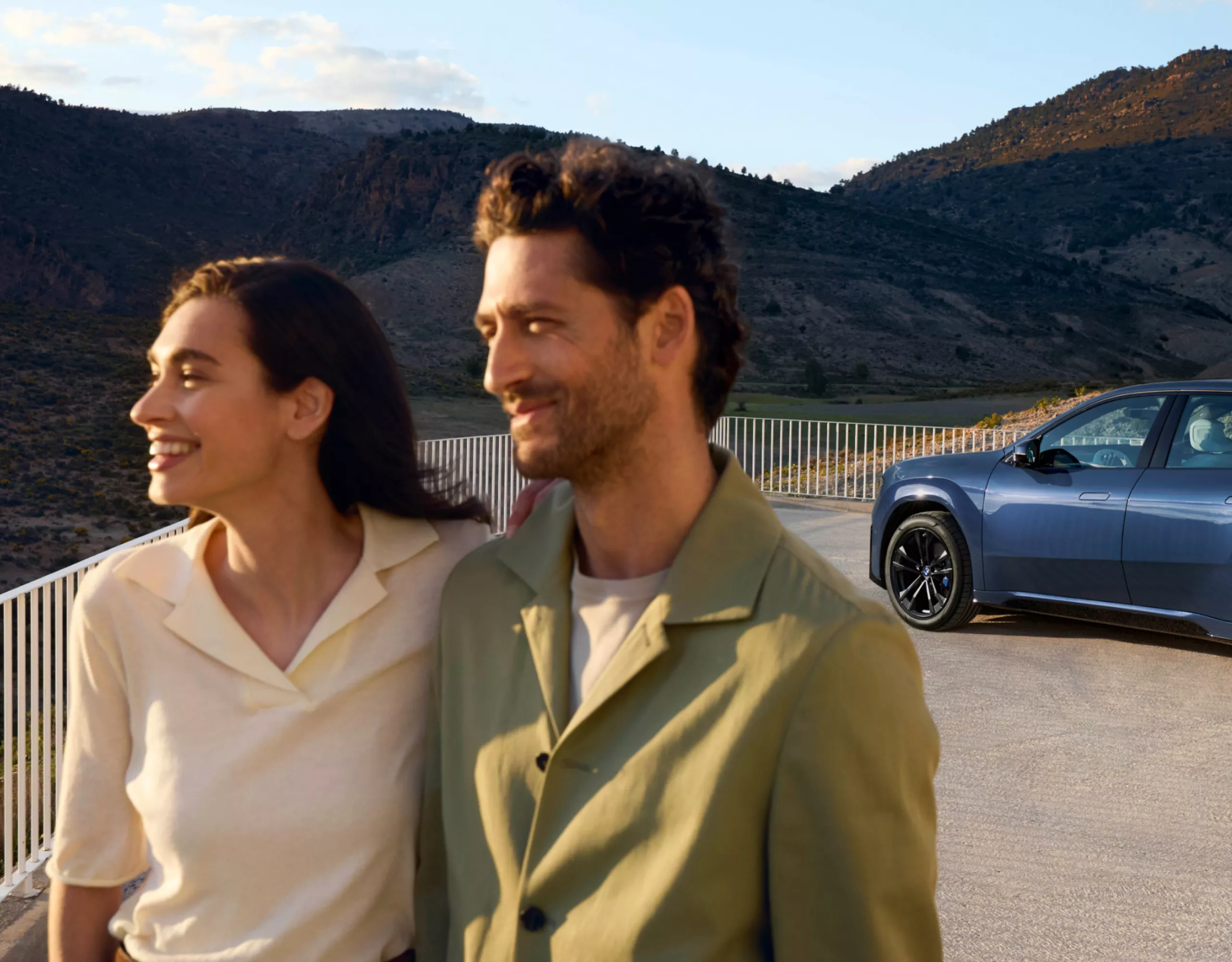 Ein BMW iX3 steht innerhalb einer Parkmarkierung am Straßenrand, der von Pflanzen gesäumt ist 