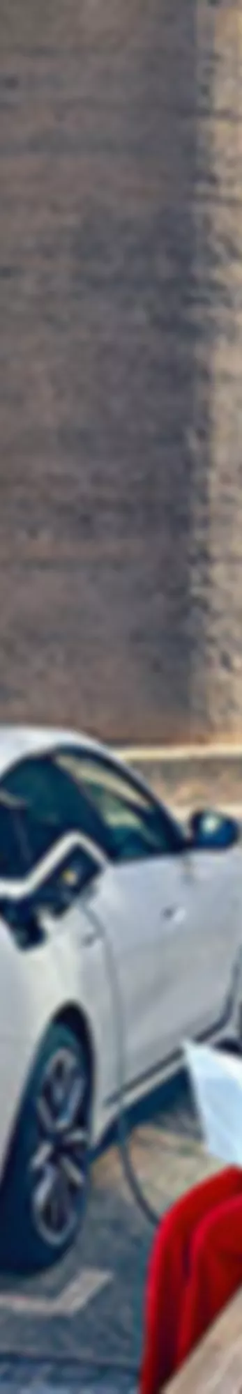 Nainen istuu penkillä kannettava tietokone sylissään, vieressä latautuu BMW i4
