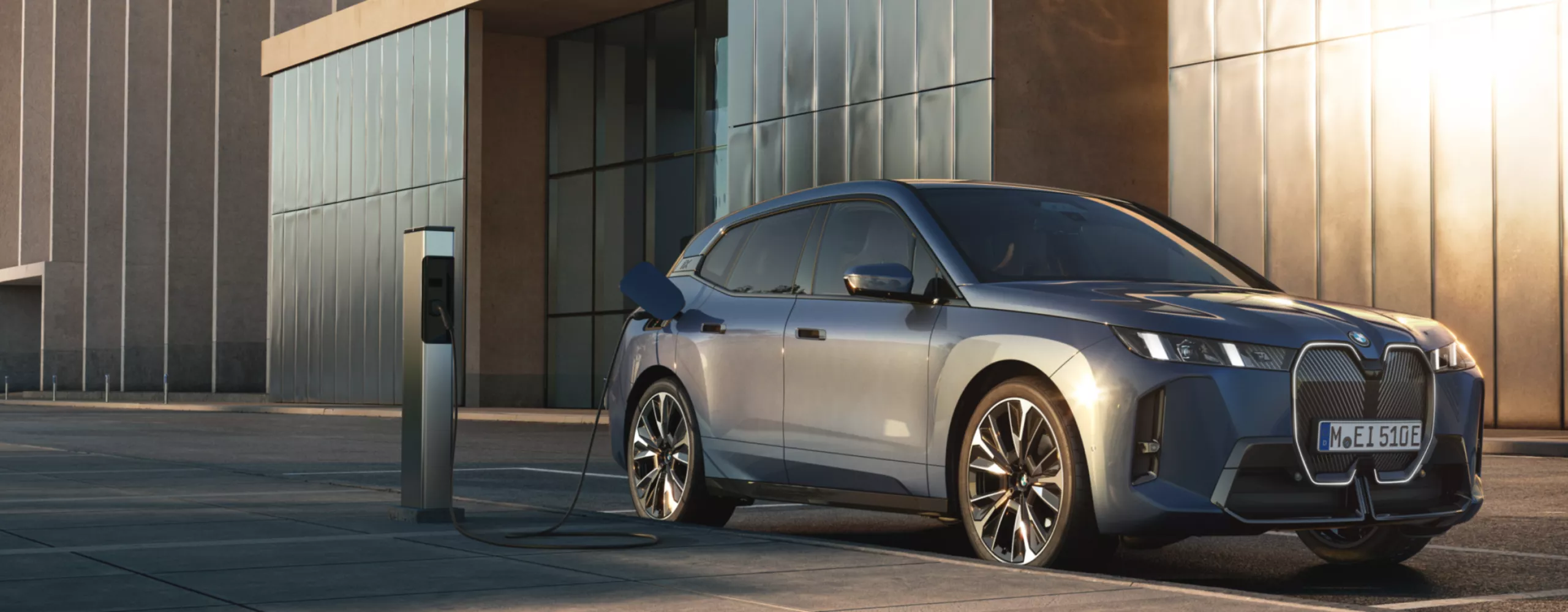  Ein BMW iX steht auf einem Parkplatz vor einem Bürogebäude und ist an einer Ladesäule angeschlossen