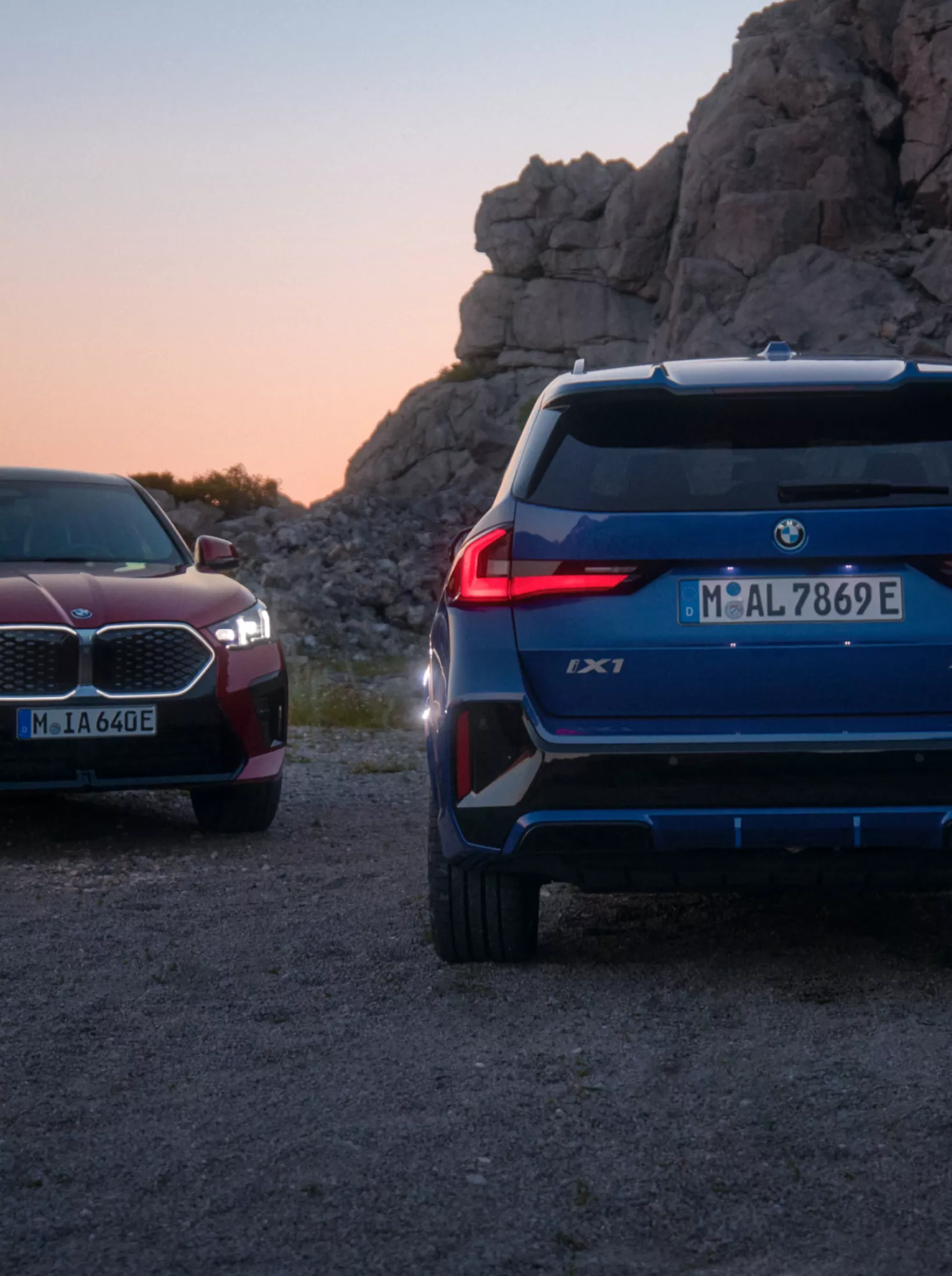 Ein BMW iX1 und ein BMW iX2 stehen bei Sonnenuntergang nebeneinander auf einem Plateau