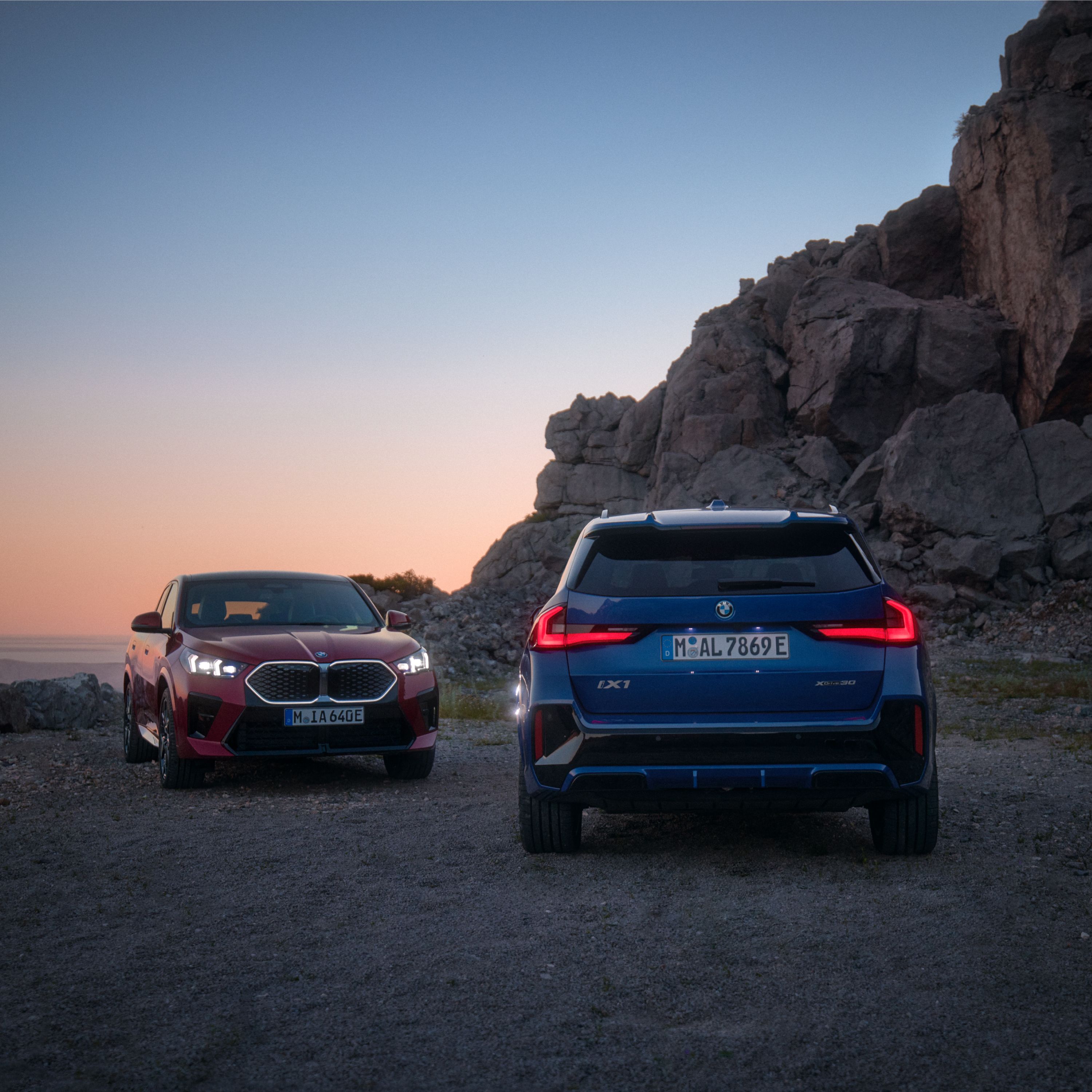 Un BMW iX1 y un BMW iX2 uno junto a otro en una meseta al atardecer