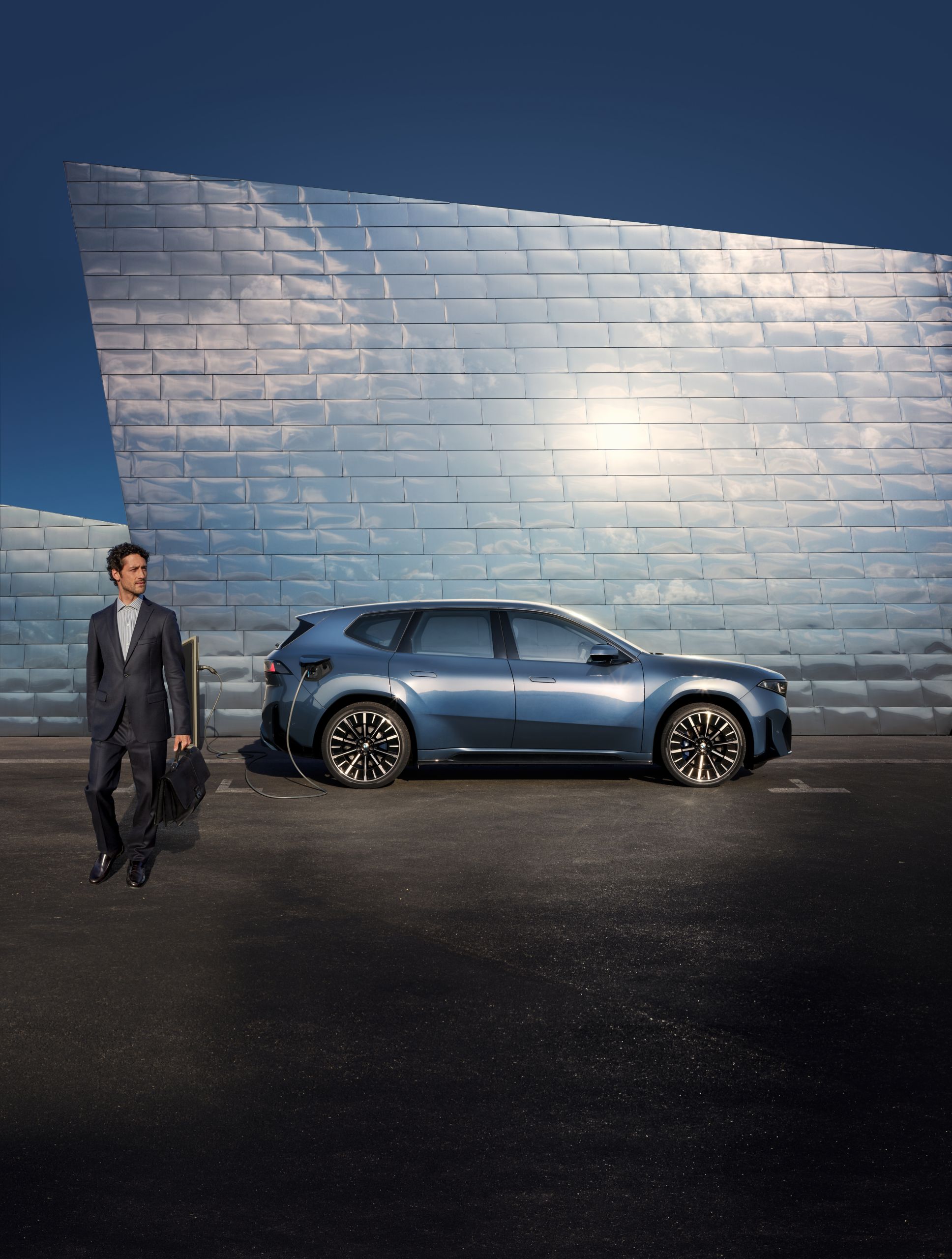 Om de afaceri îndepărtându-se de un automobil de companie BMW iX3 albastru, parcat în fața unei fațade moderne din metal