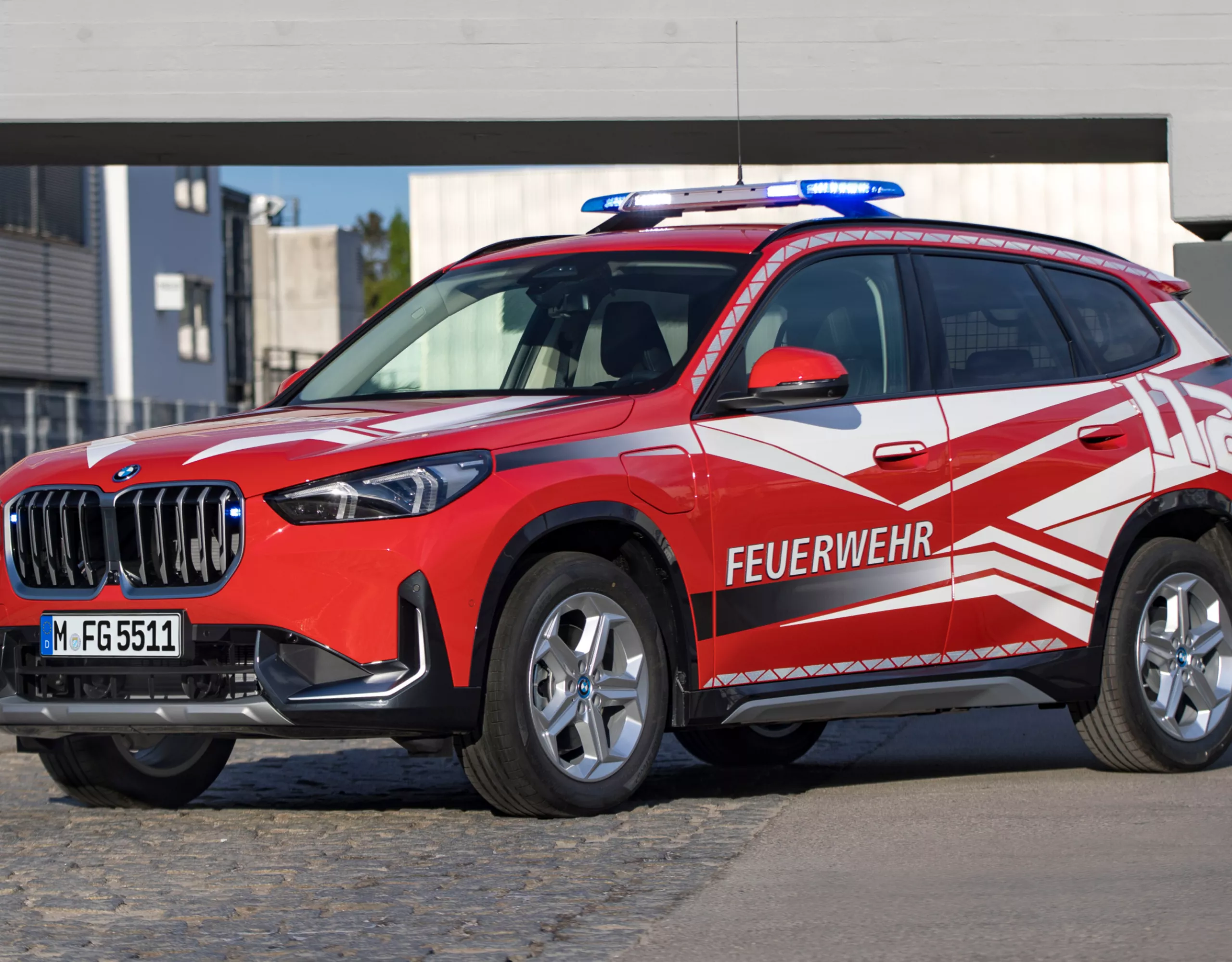 A BMW fire-fighting vehicle parked in front of a modern building beneath a concrete bridge