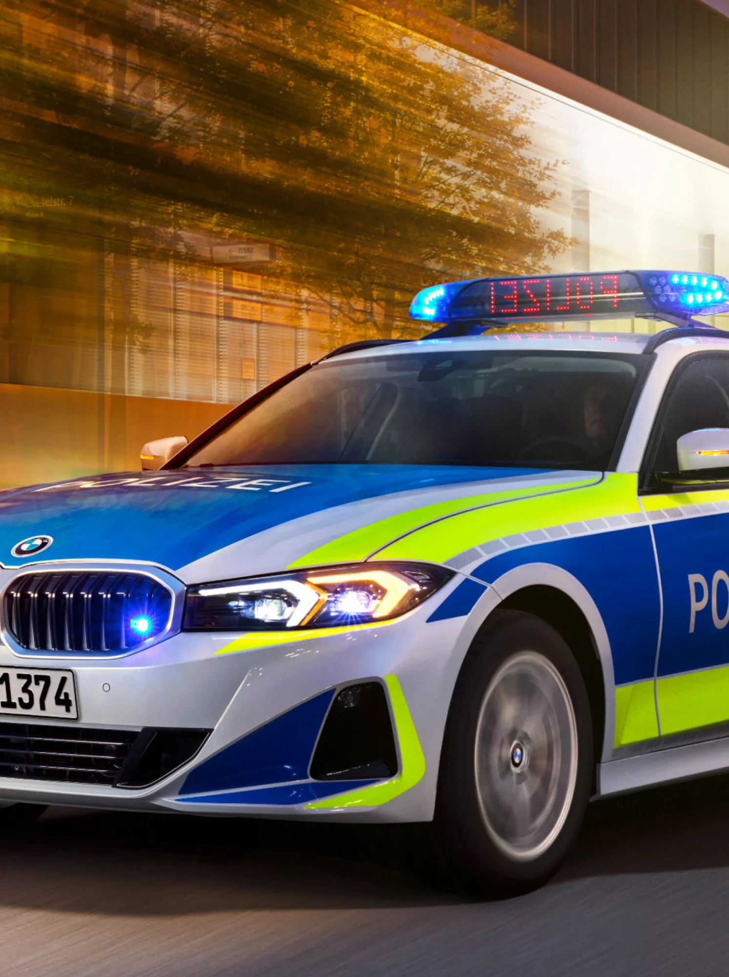 A BMW police vehicle drives past a lit-up building by twilight