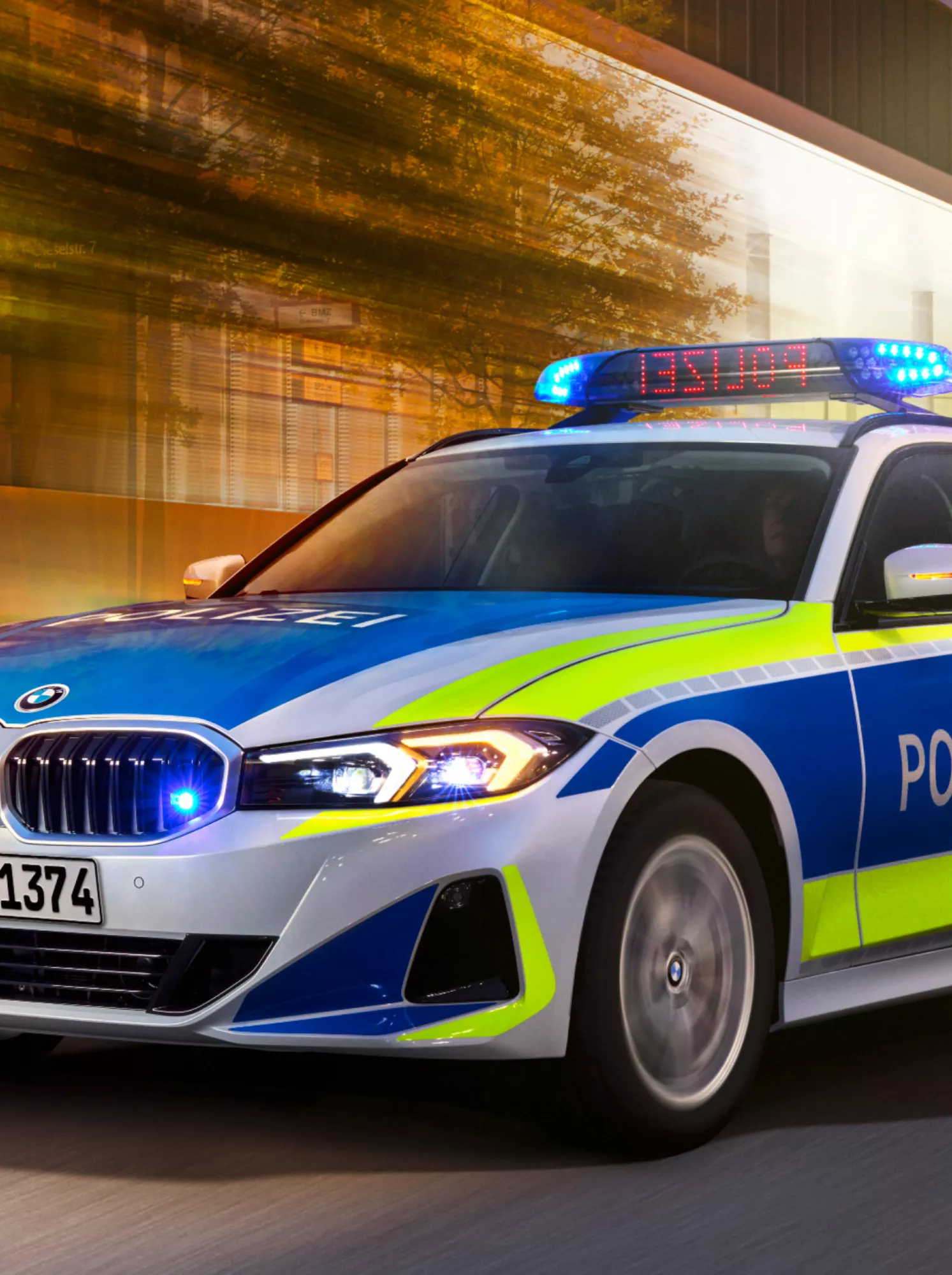 Een BMW politiewagen rijdt in de schemering langs een verlicht gebouw