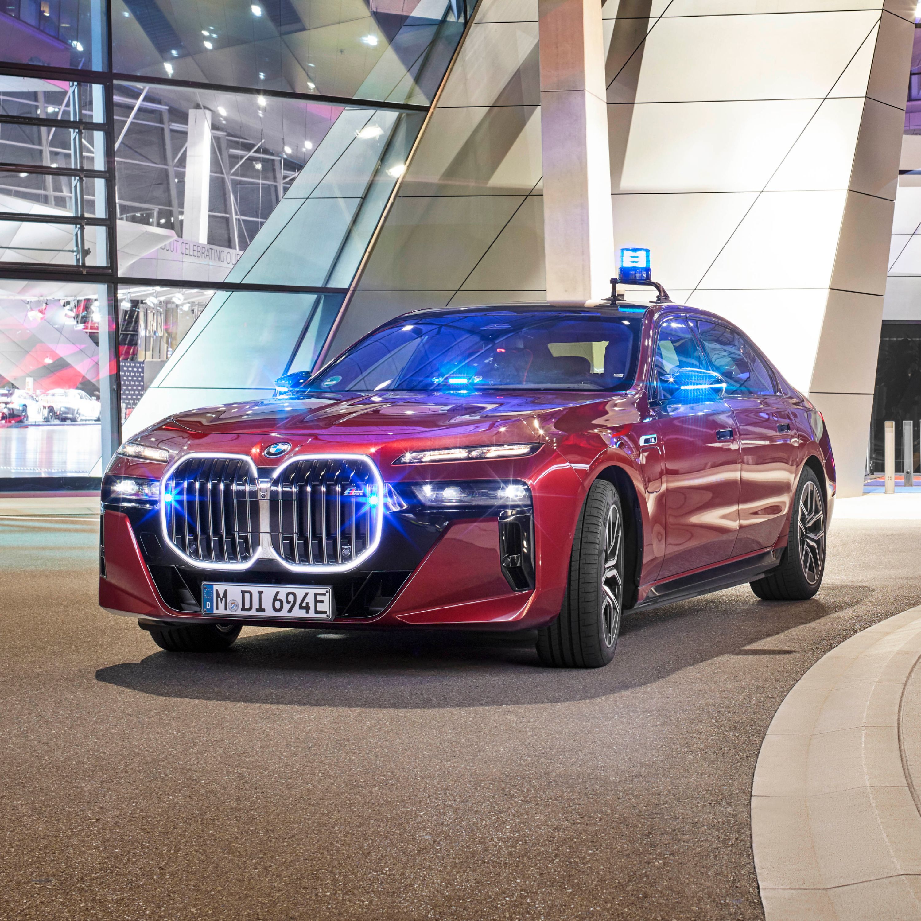 A BMW fire brigade vehicle parked in front of a modern building illuminated in pink and purple